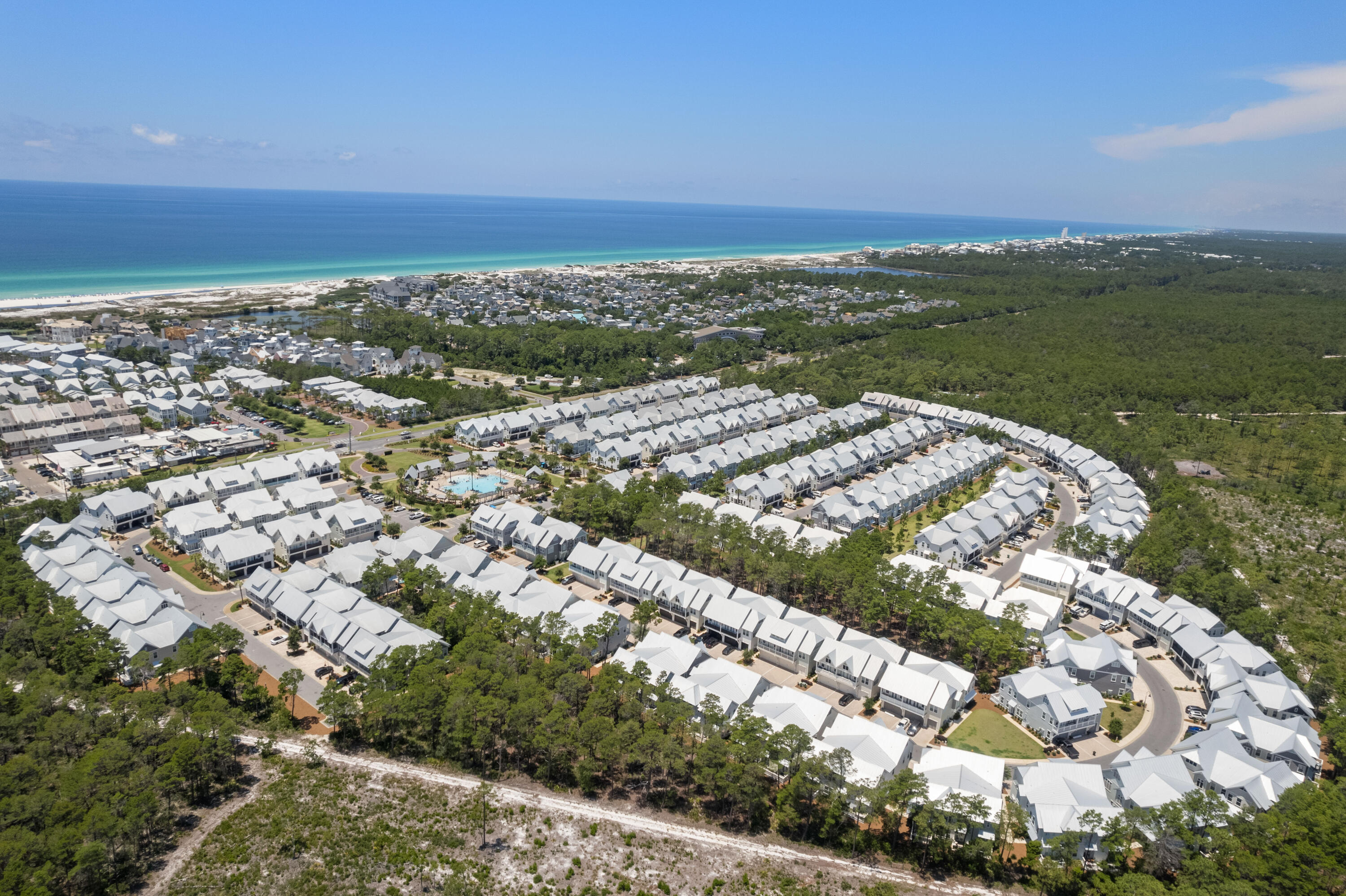 Aerial view of coastal townhomes, a community pool, pine forest, and Gulf beach.