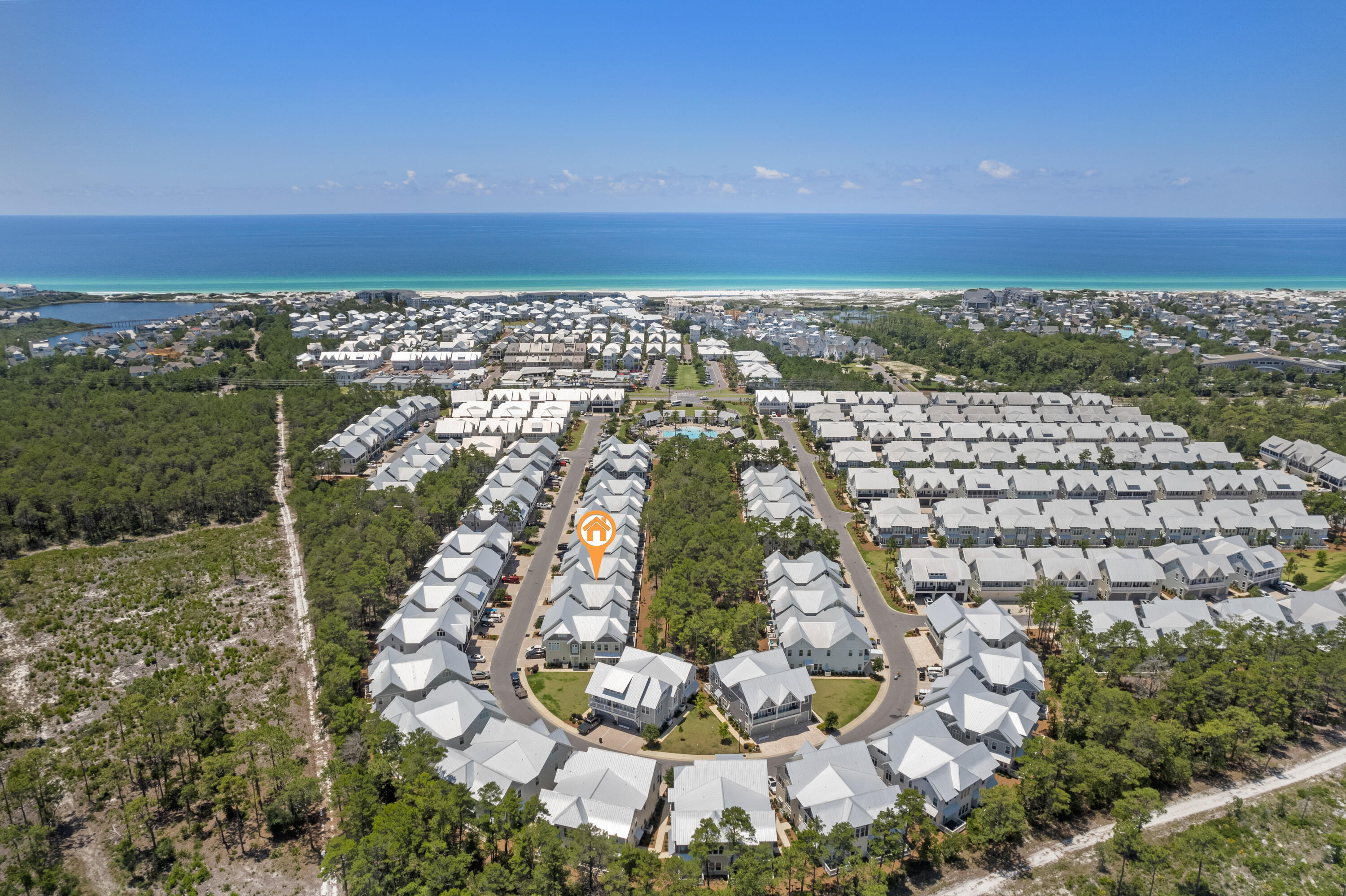 Aerial view of coastal homes with an orange marker, shared pool, and ocean beyond.