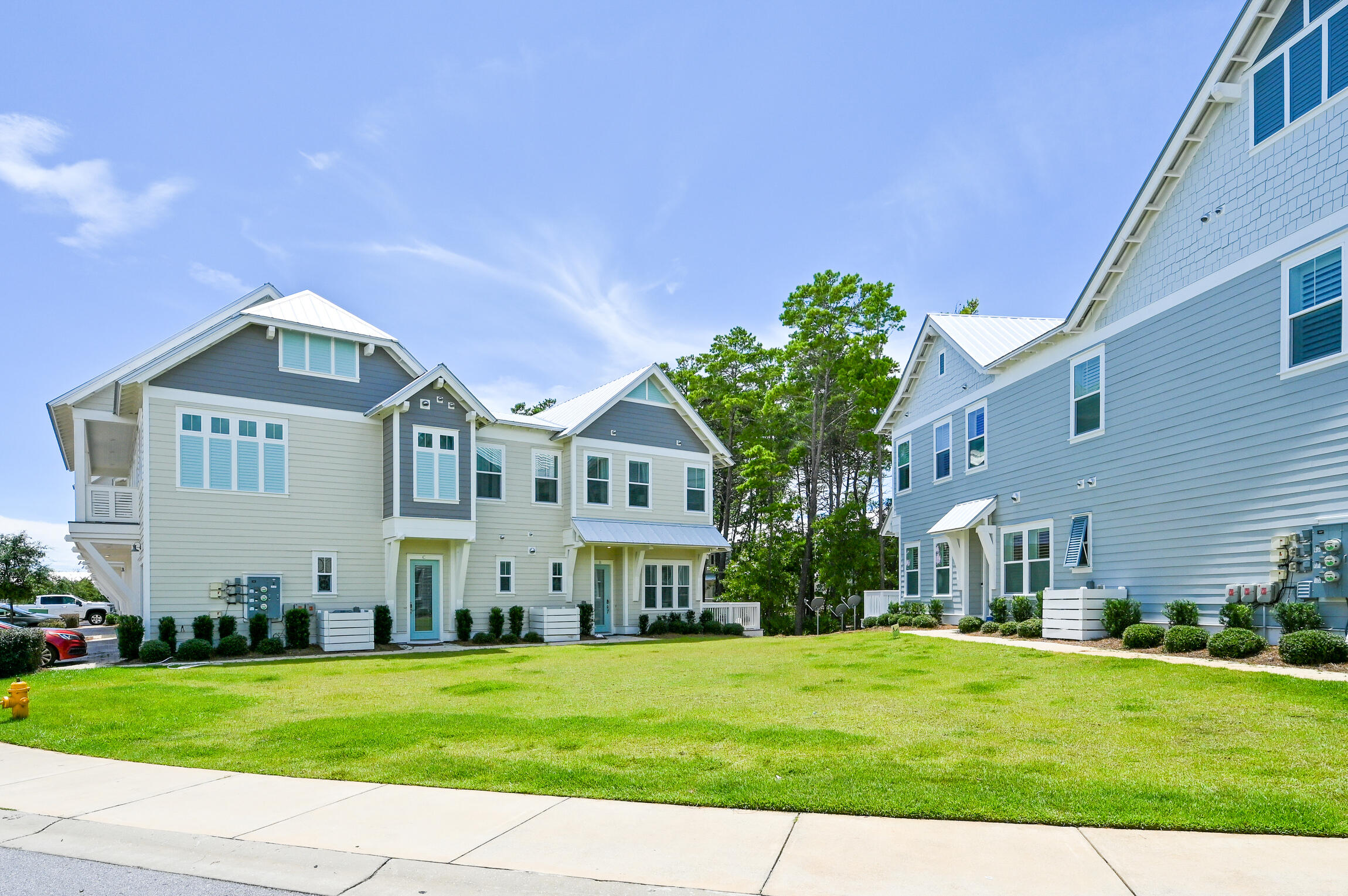 Blue-gray townhomes with white trim flank a green lawn and sidewalk.