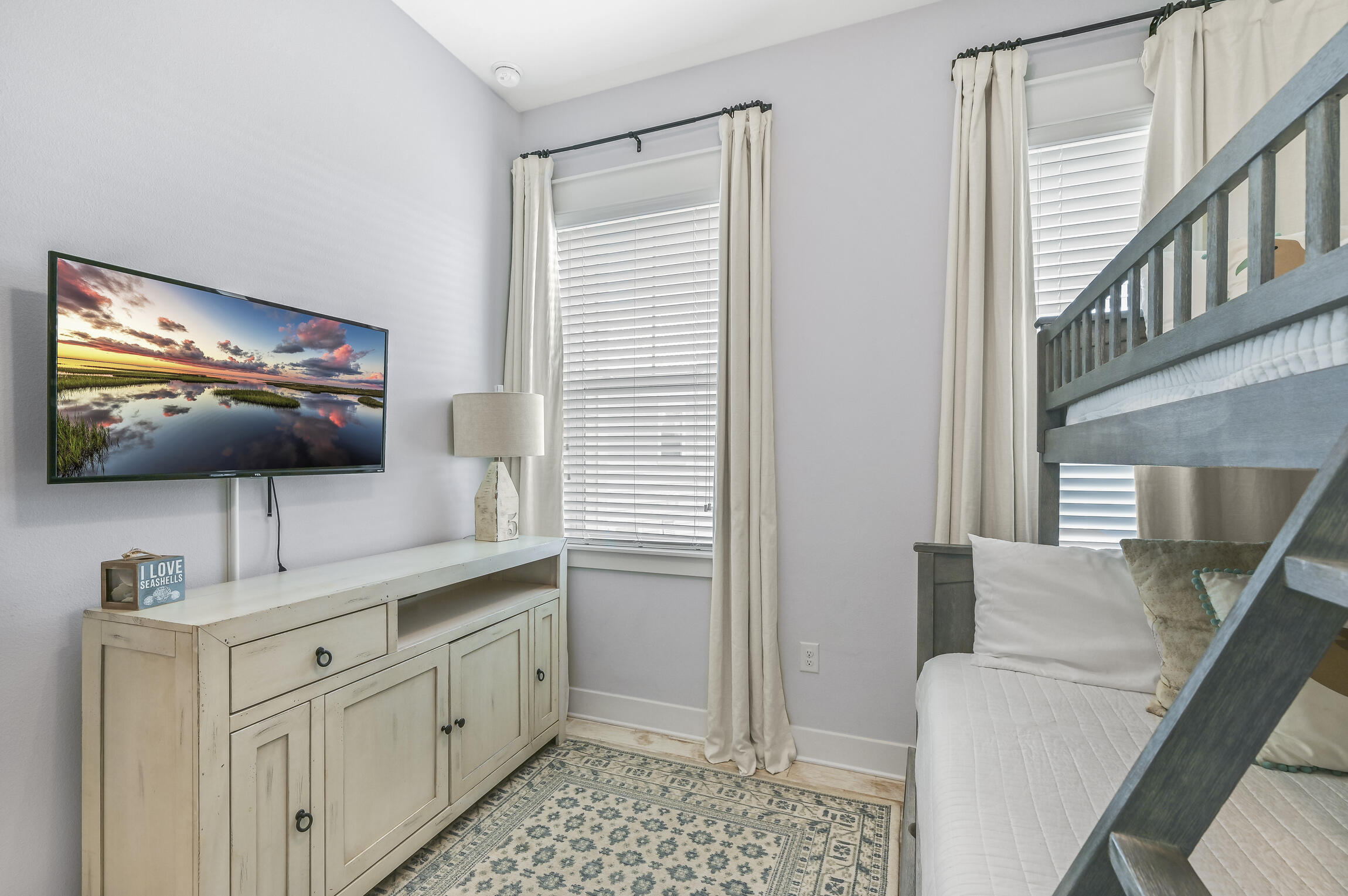 Bedroom with a gray wooden bunk bed, wall-mounted TV, and distressed white dresser.