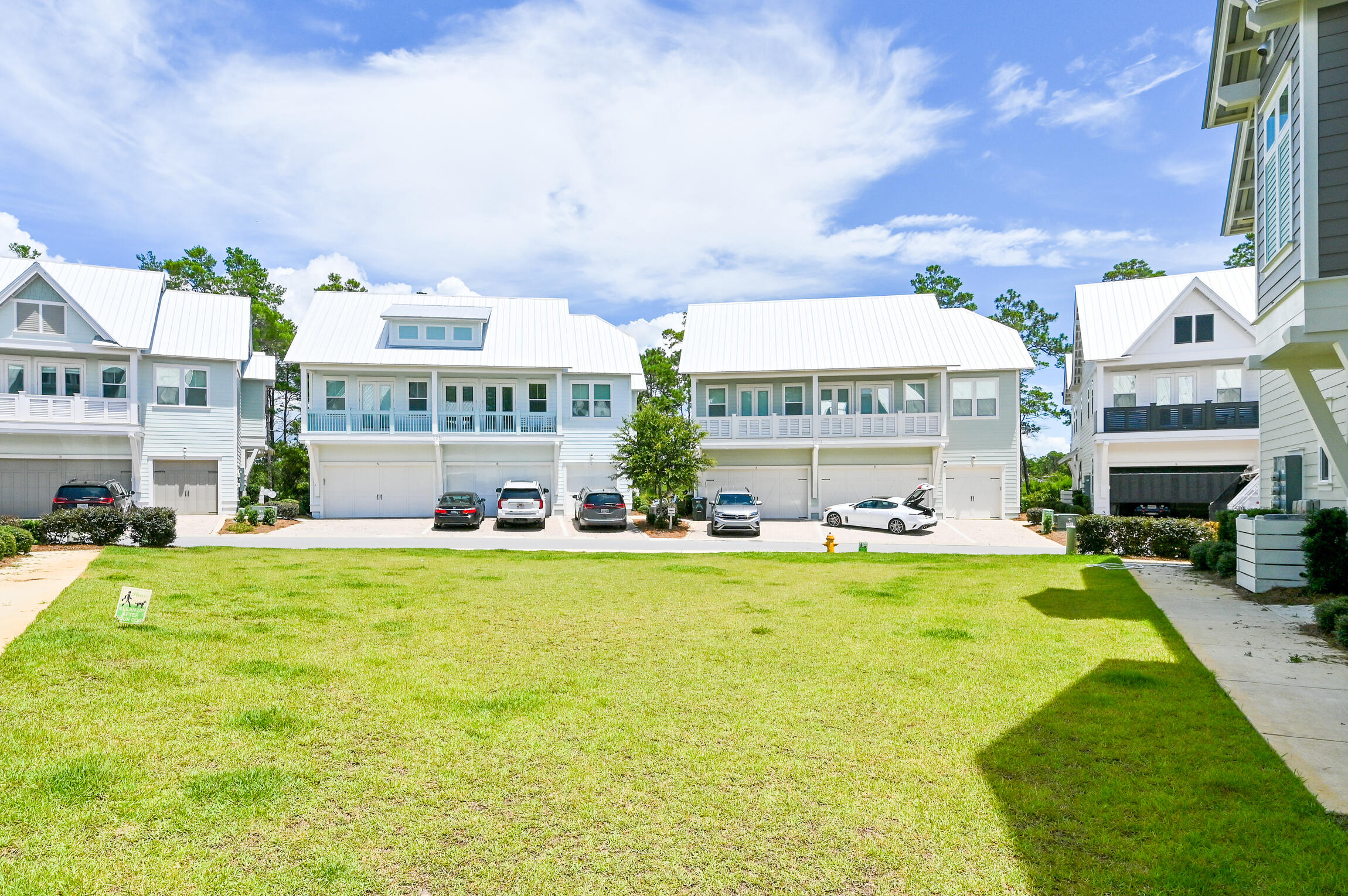 Coastal-style homes with white metal roofs and balconies beyond a broad green lawn.