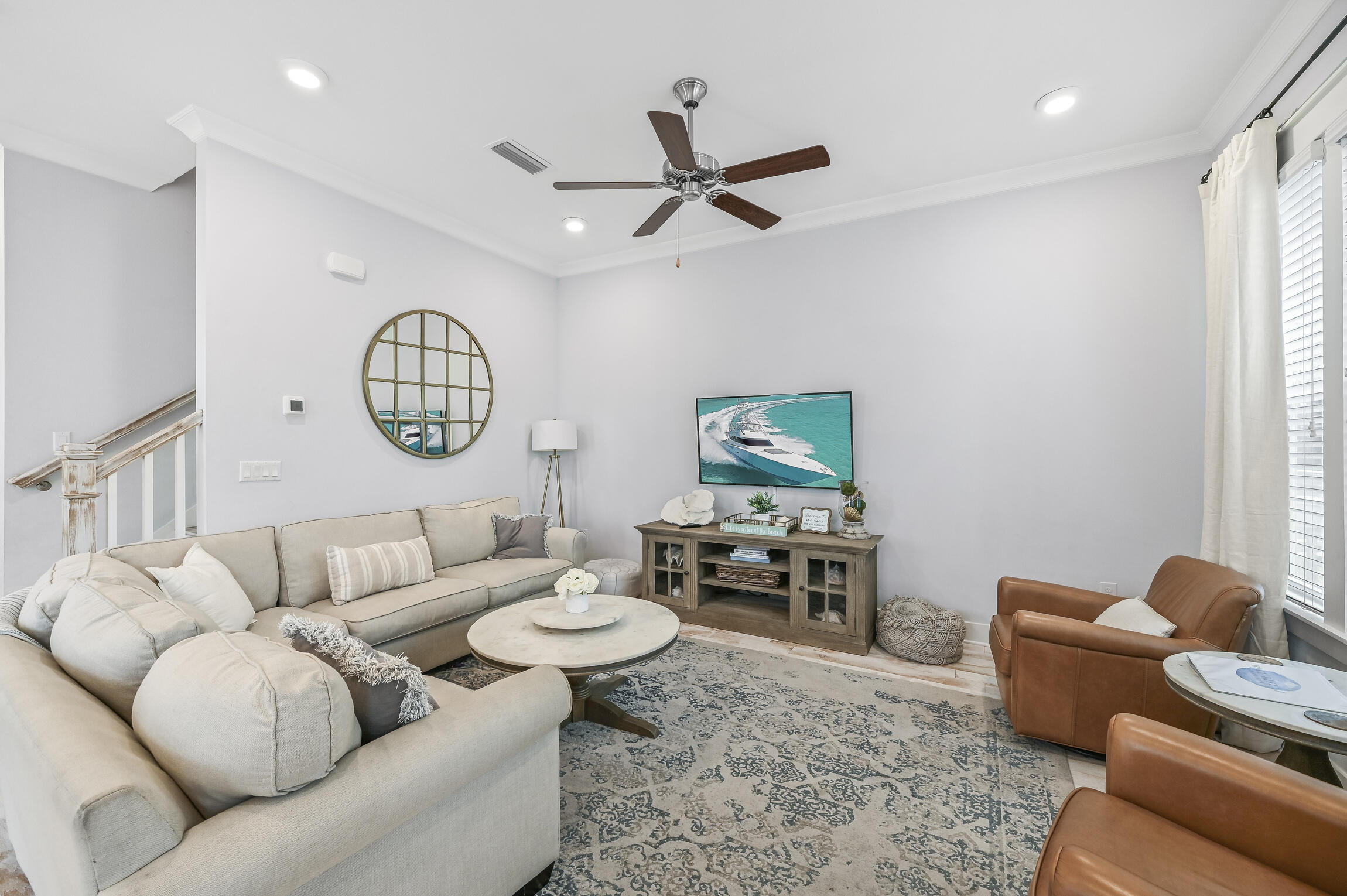 Furnished living room with a cream sectional, leather armchairs, patterned rug, and TV showing a boat.