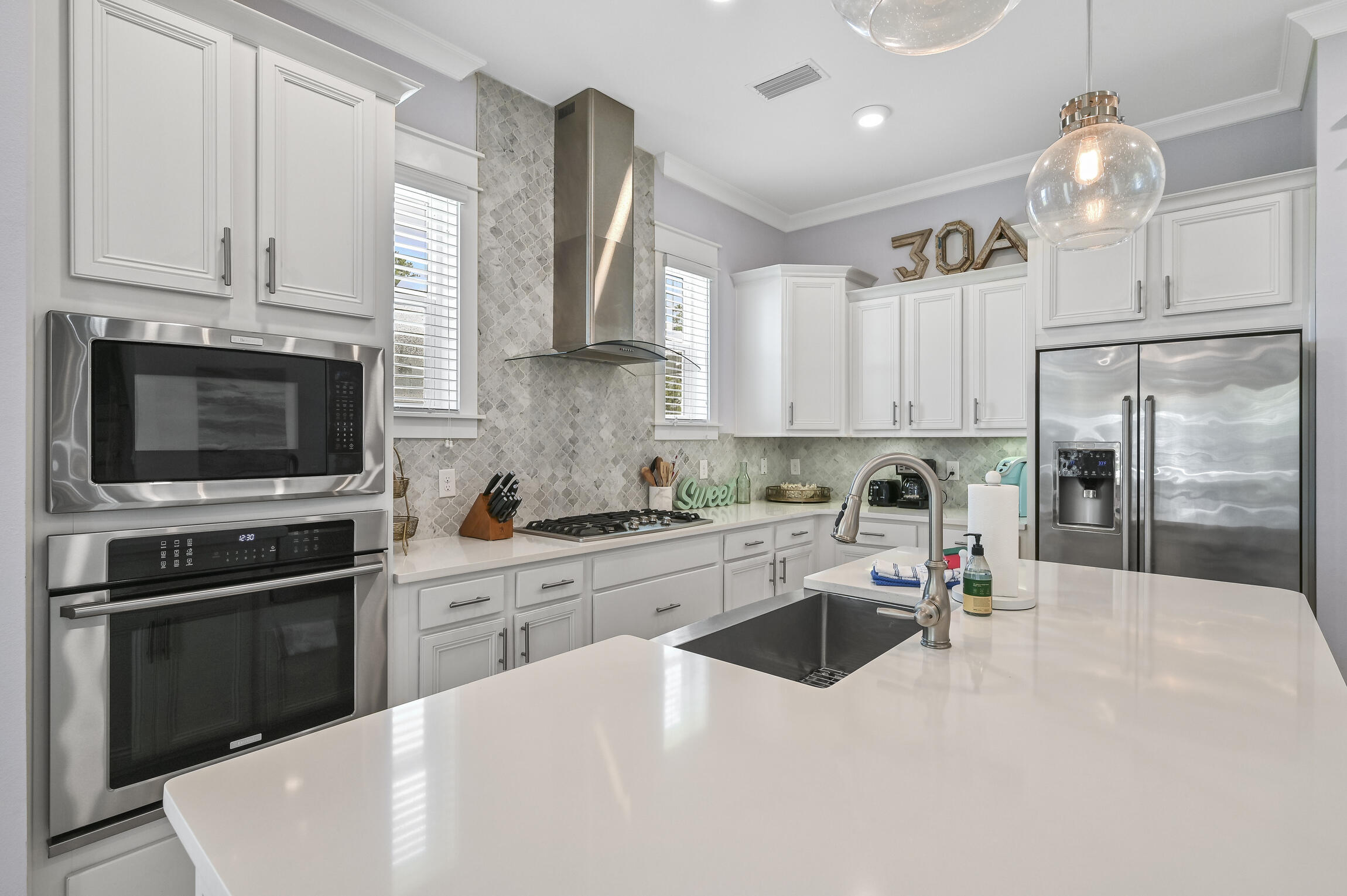 Kitchen with white cabinets, stainless appliances, patterned backsplash, and a large island with a dark sink.