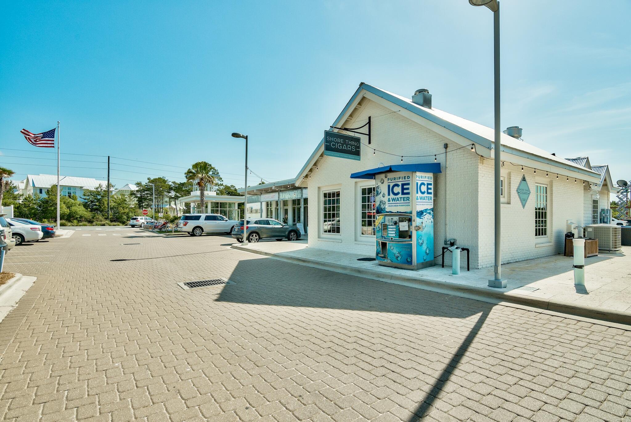 White-brick Shore Thing Cigars storefront with a blue ice-and-water vending machine beside the paved parking area.