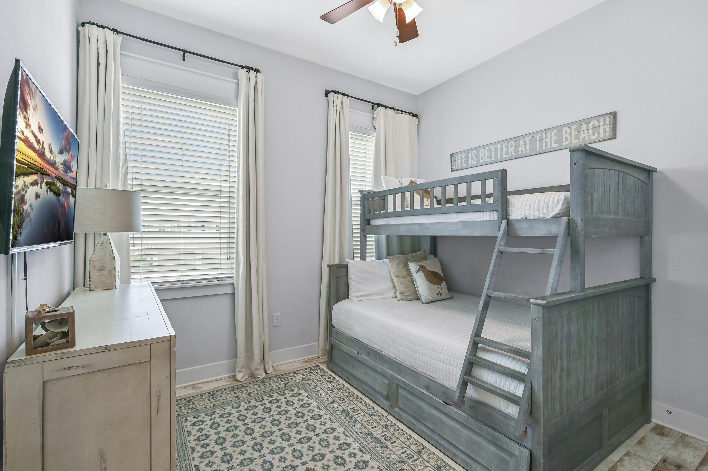 Bedroom with a gray wooden bunk bed, built-in ladder, and beach-themed sign.