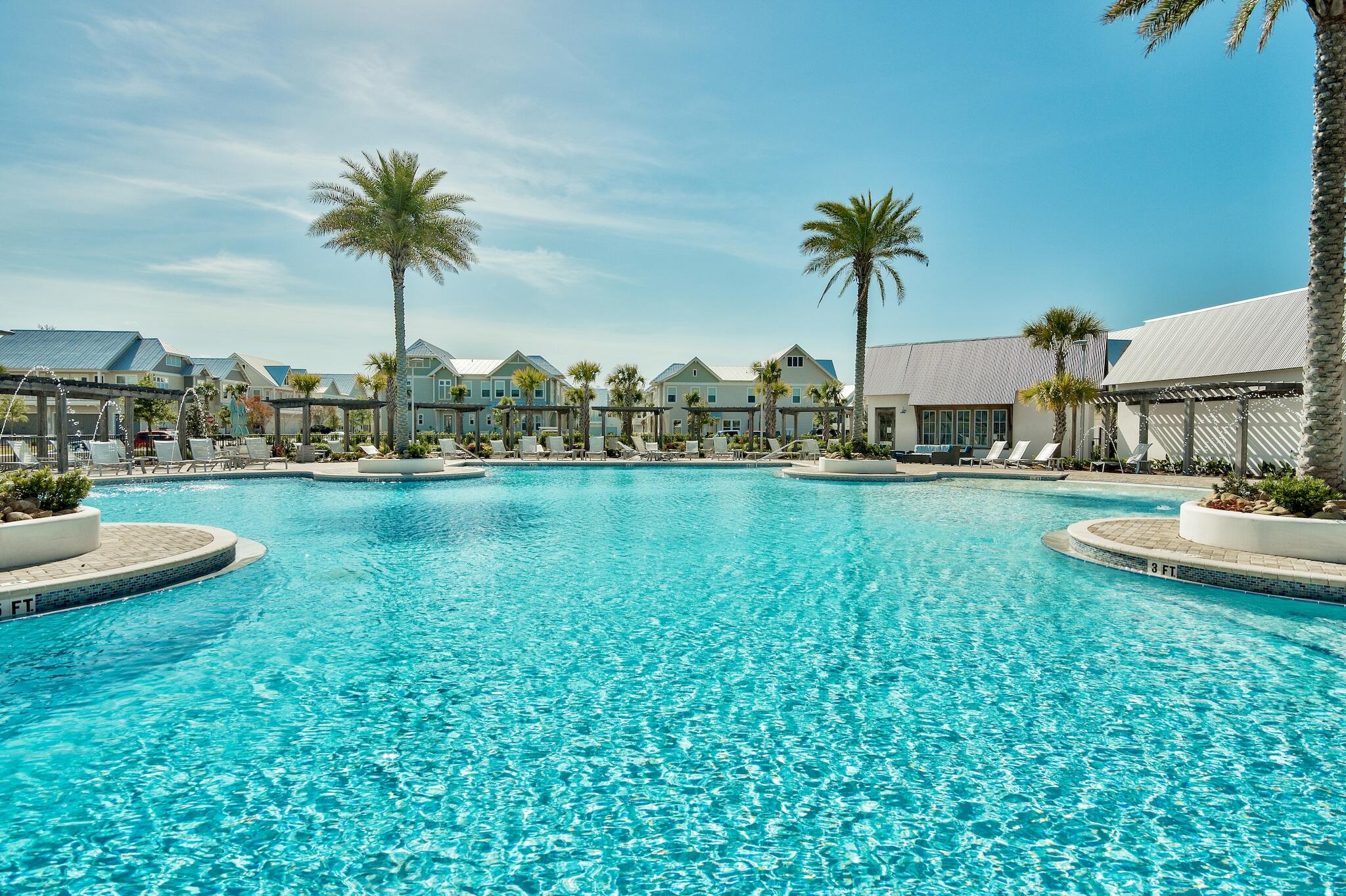 Community pool surrounded by palm trees, lounge chairs, and coastal-style homes.