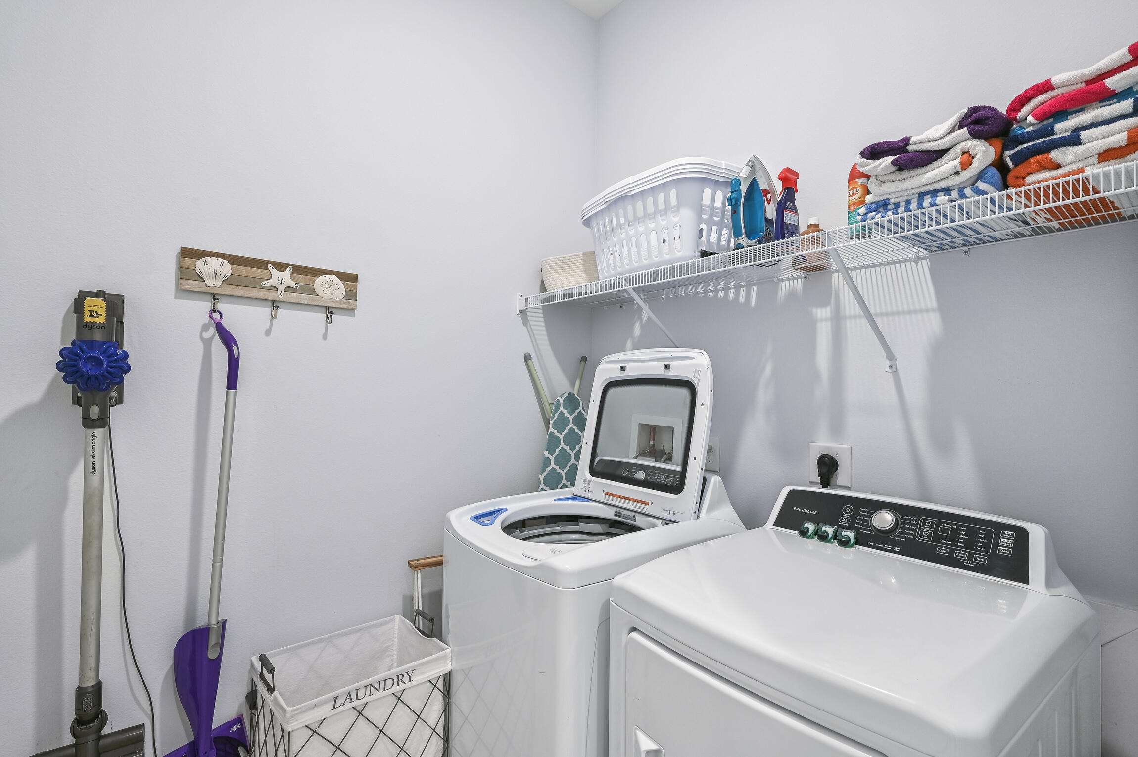 Laundry room with washer and dryer beneath a shelf of folded towels and cleaning supplies.