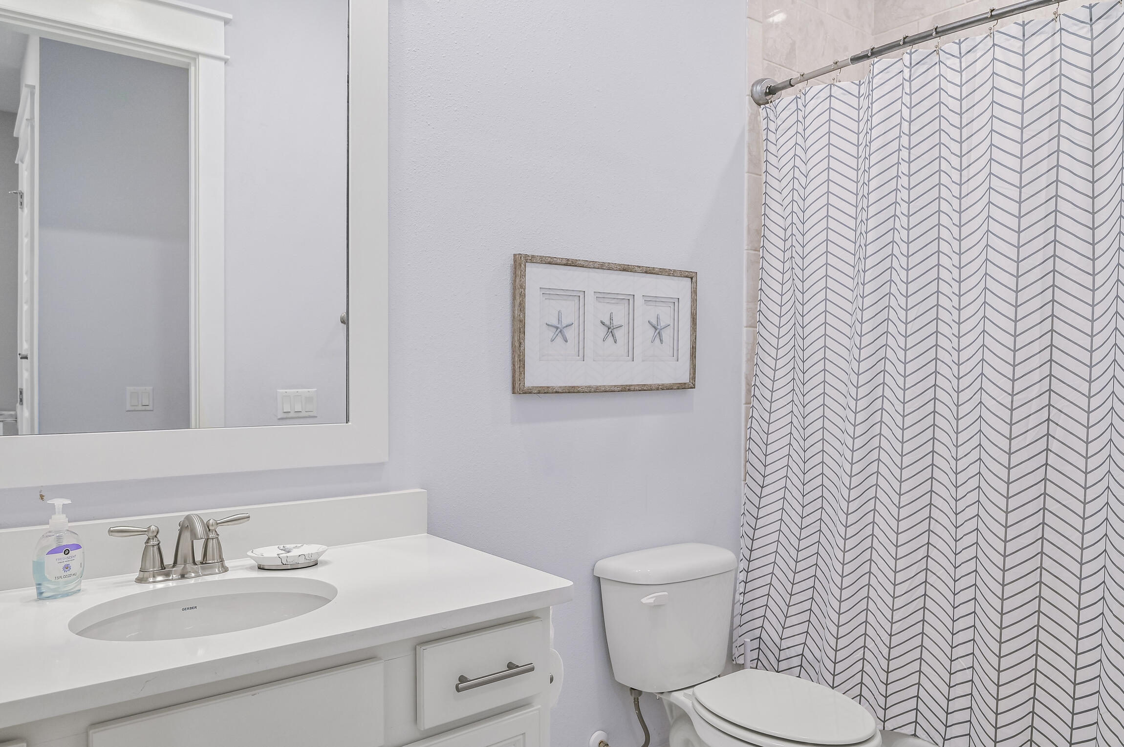 Bathroom with white vanity, toilet, and gray chevron shower curtain beside framed starfish art.