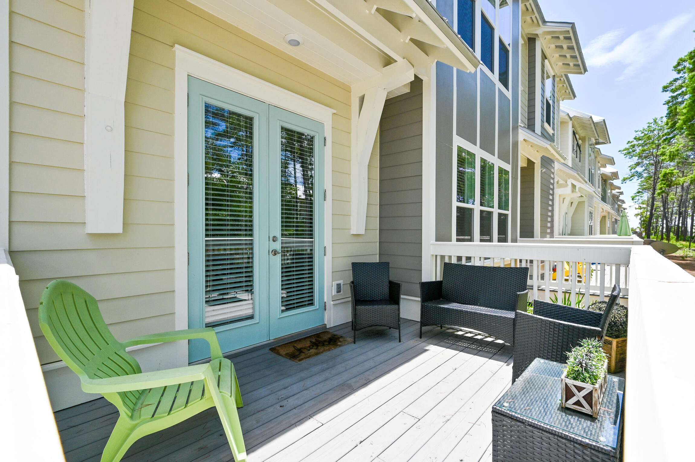 Covered deck with pale blue doors, a lime-green chair, and black wicker seating.