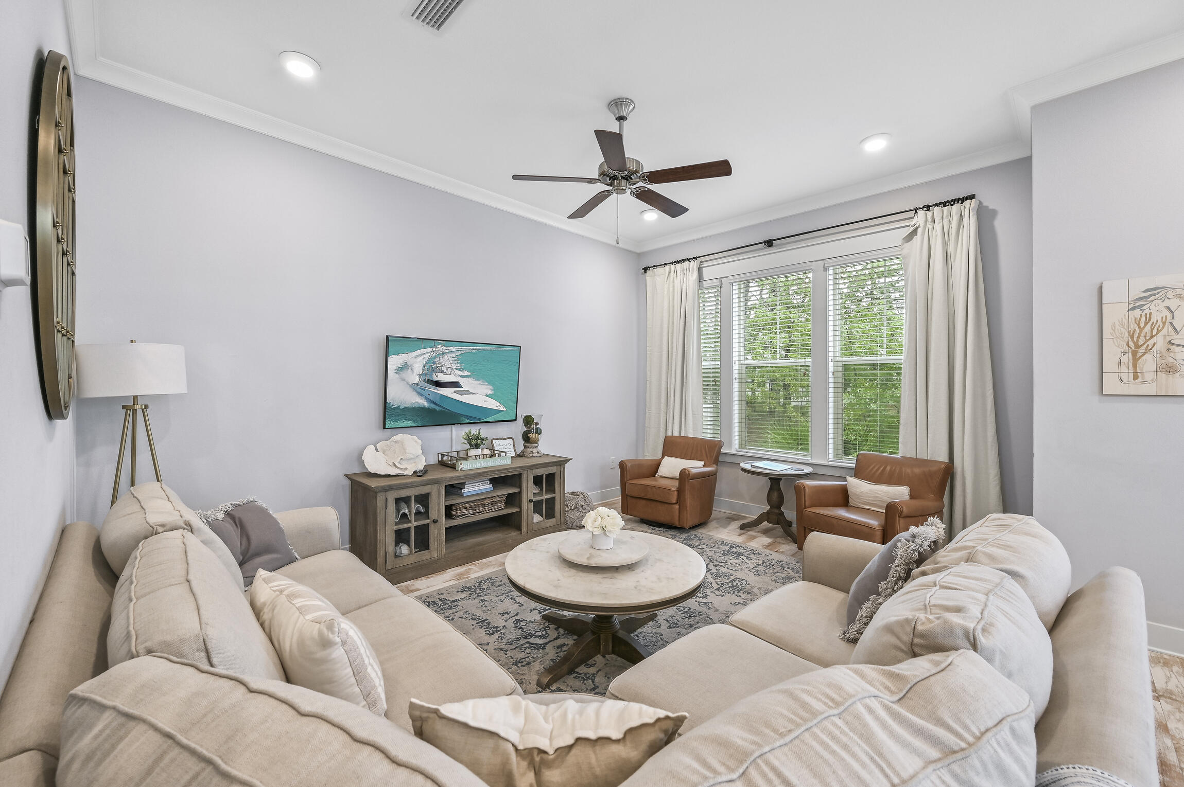 Furnished living room with pale sofas, brown leather armchairs, and a wide window with white blinds.