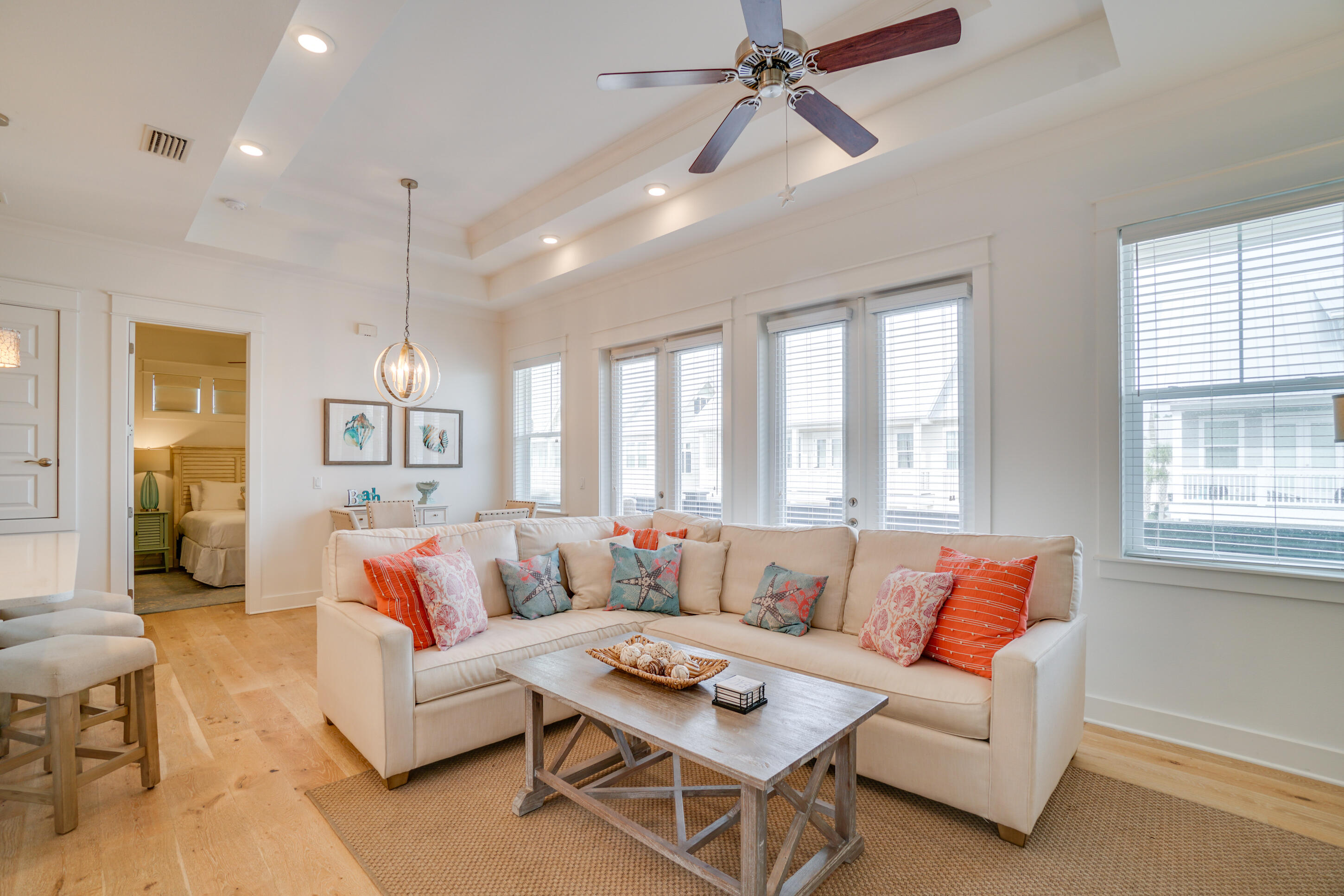Living room with a cream sectional, coastal pillows, wood coffee table, and tall windows with blinds.
