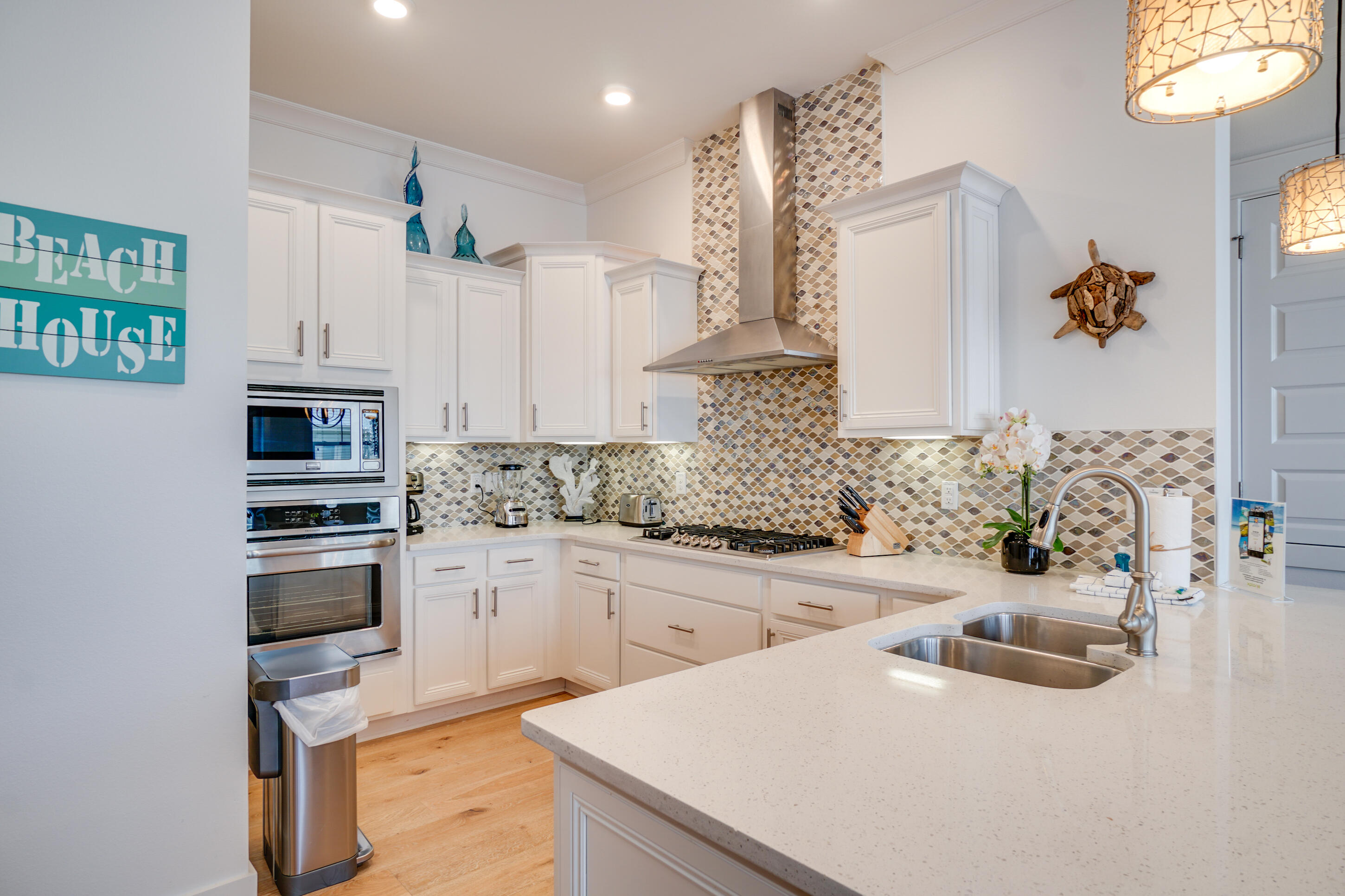 Kitchen with white cabinets, patterned tile backsplash, stainless appliances, and a large island with double sink.