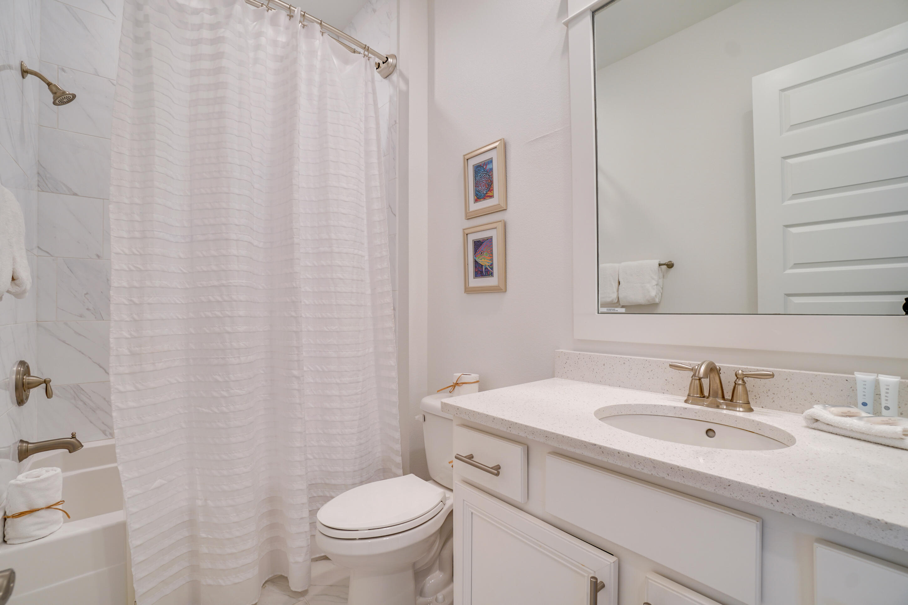 Bathroom with marble-look tub surround, white vanity, large mirror, and brass-toned fixtures.