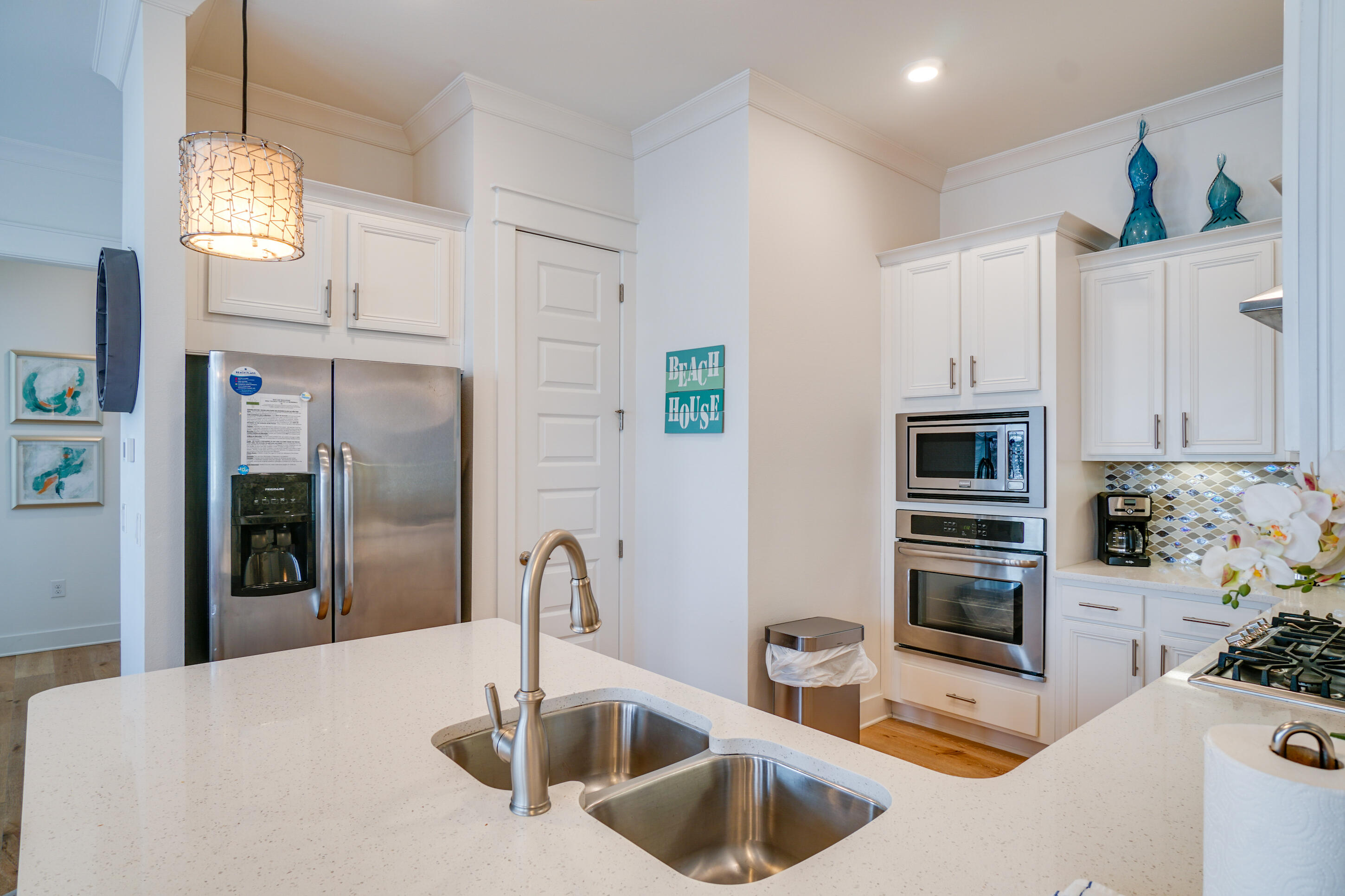 Bright white kitchen with stainless steel appliances, mosaic backsplash, and a large island with double sink.