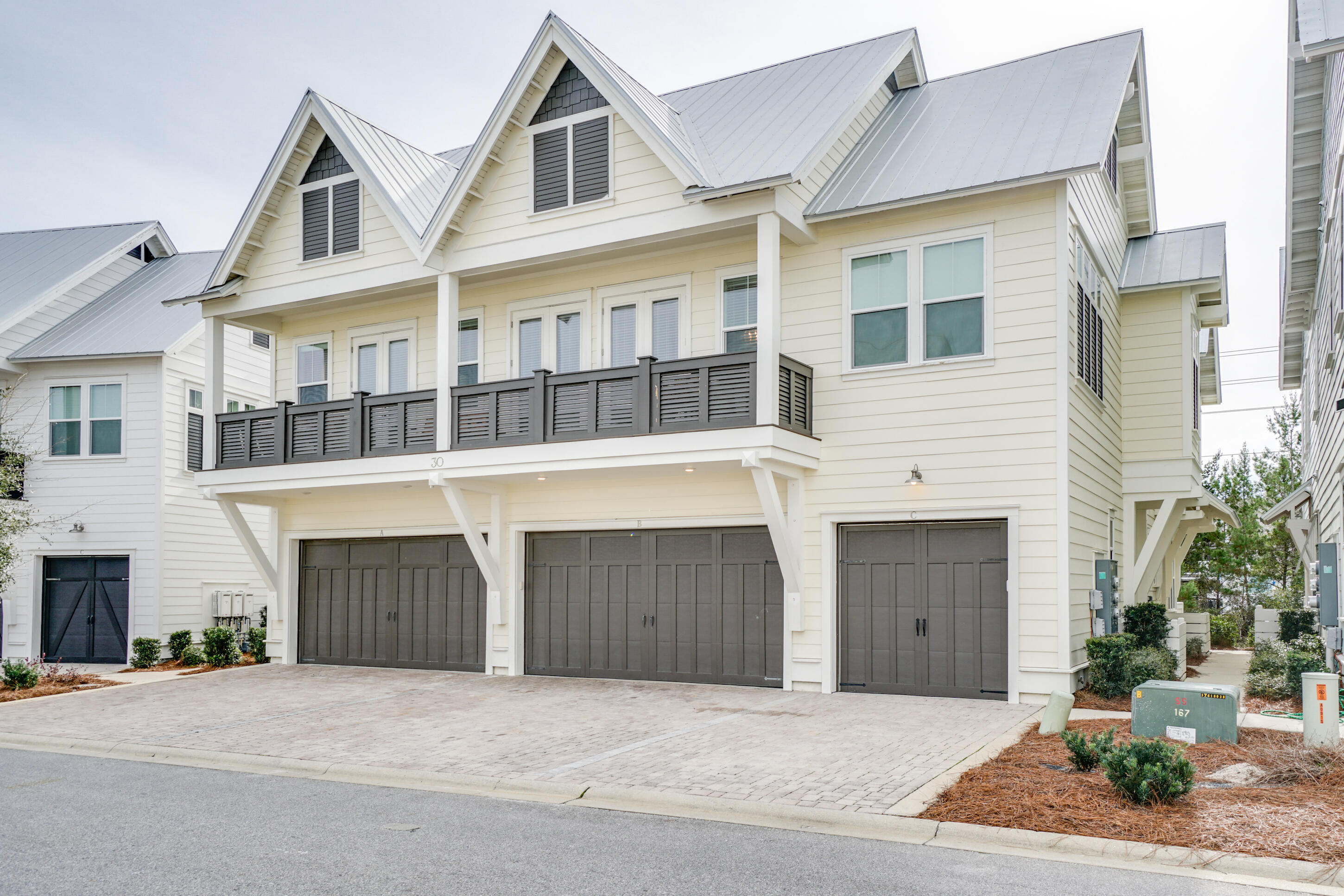 Cream coastal-style residence with a dark-railed balcony, metal roofs, and three garage doors.