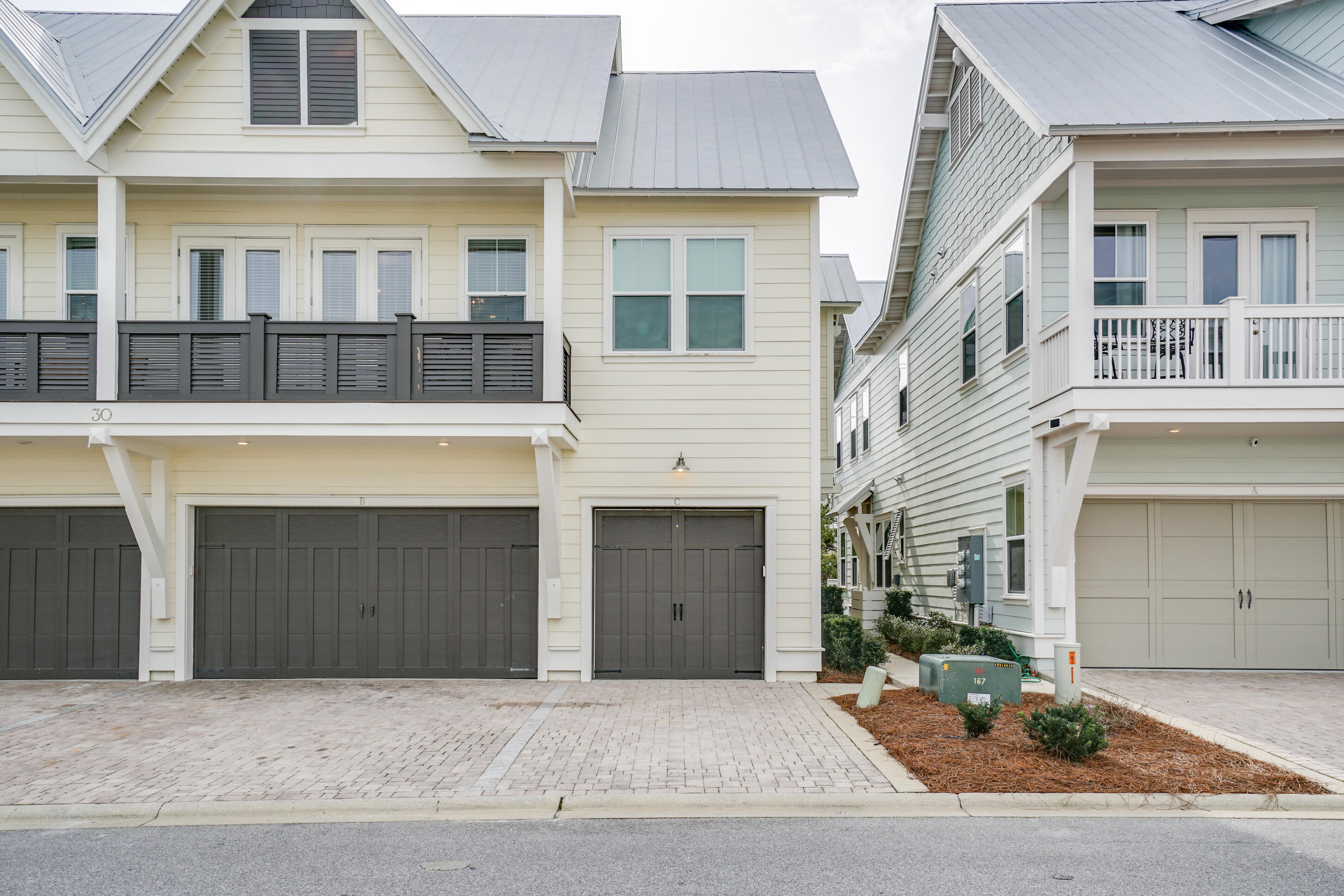 Cream coastal-style home with gray metal roof, upper balcony, and garage marked C beside a neighboring home.
