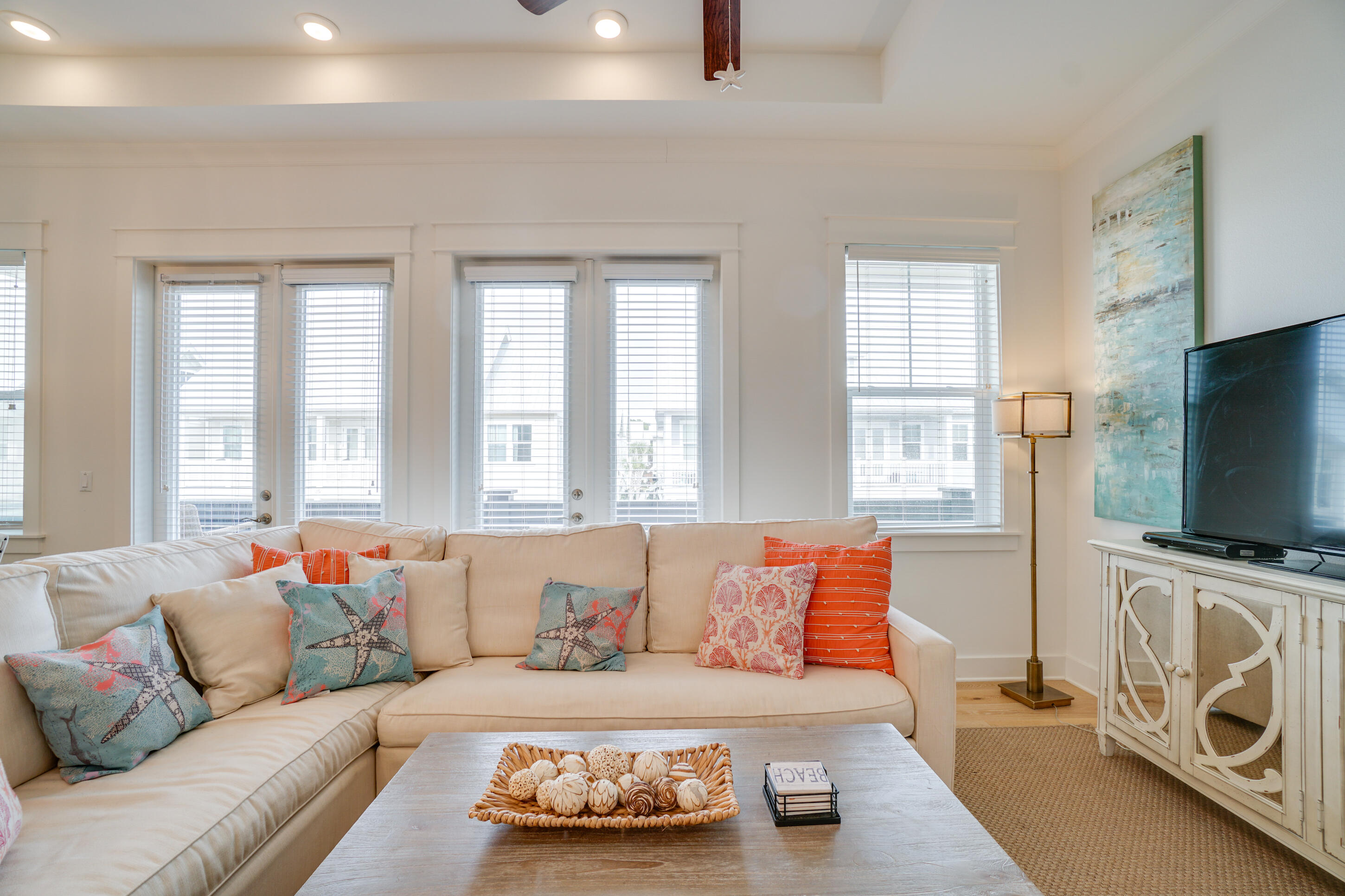Living room with a cream sectional, colorful coastal pillows, and large bright windows.