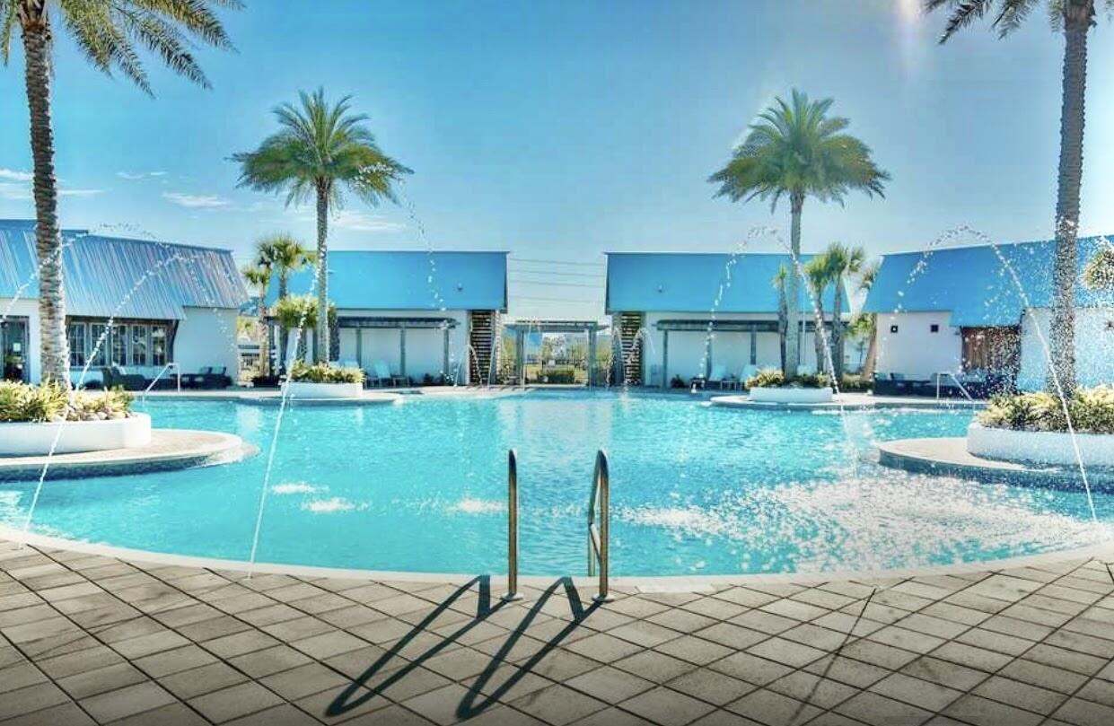 Community pool with fountains, palm trees, and modern buildings along the far side.
