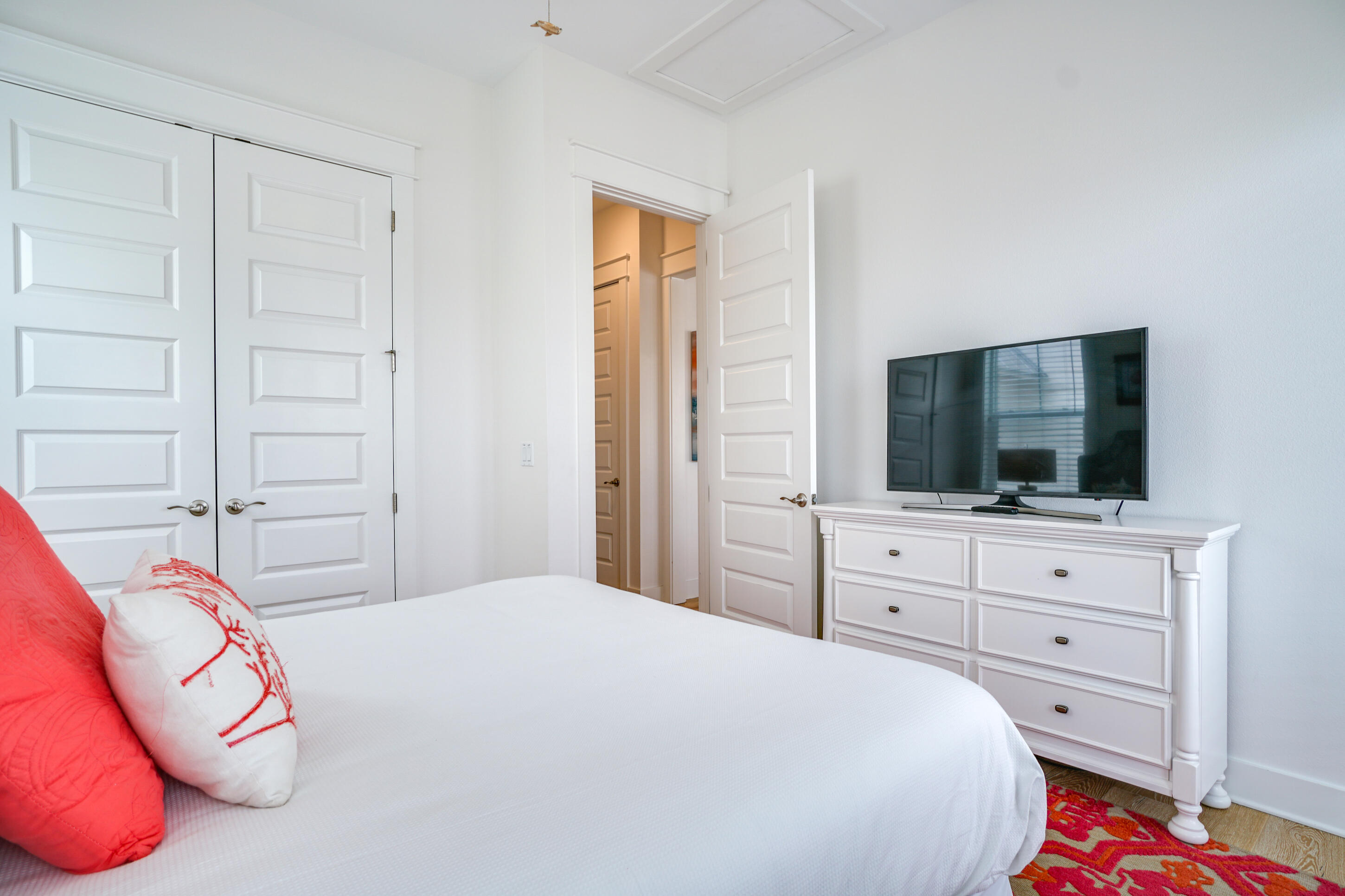 Bedroom with a white bed, coral pillows, and a television on a white dresser.