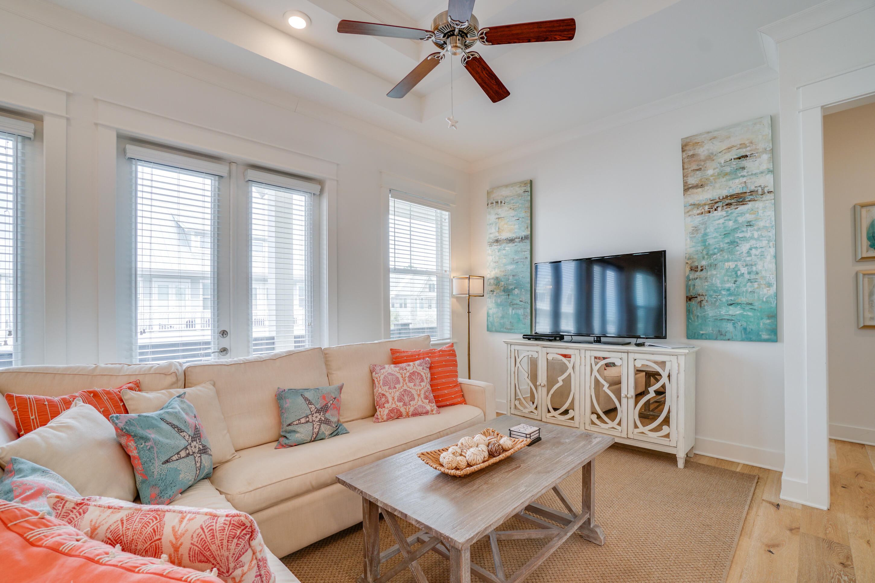 Bright living room with a cream sofa, coastal-patterned pillows, and a television above a white console.
