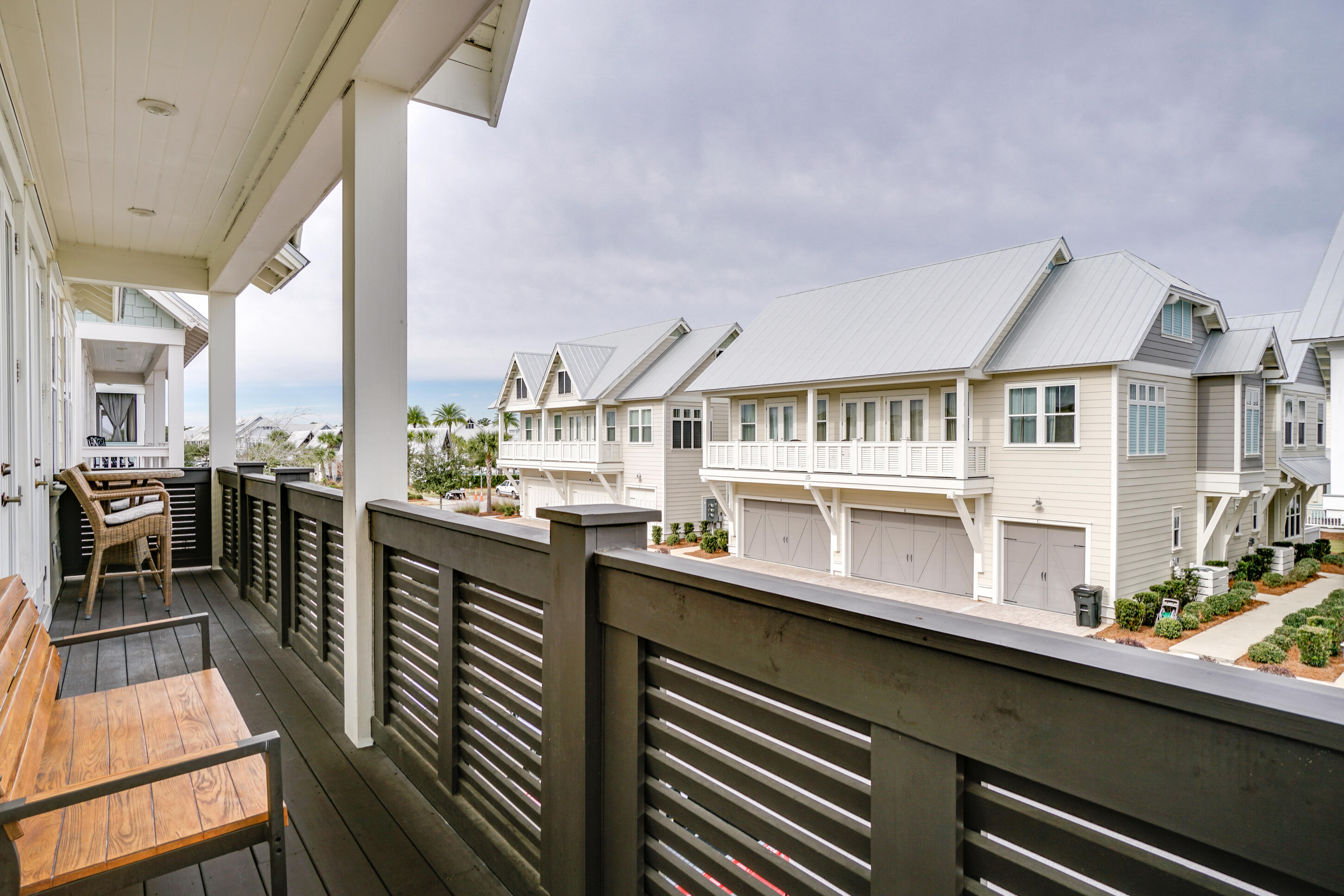 Covered balcony with wooden seating overlooks light-colored coastal homes with white metal roofs.