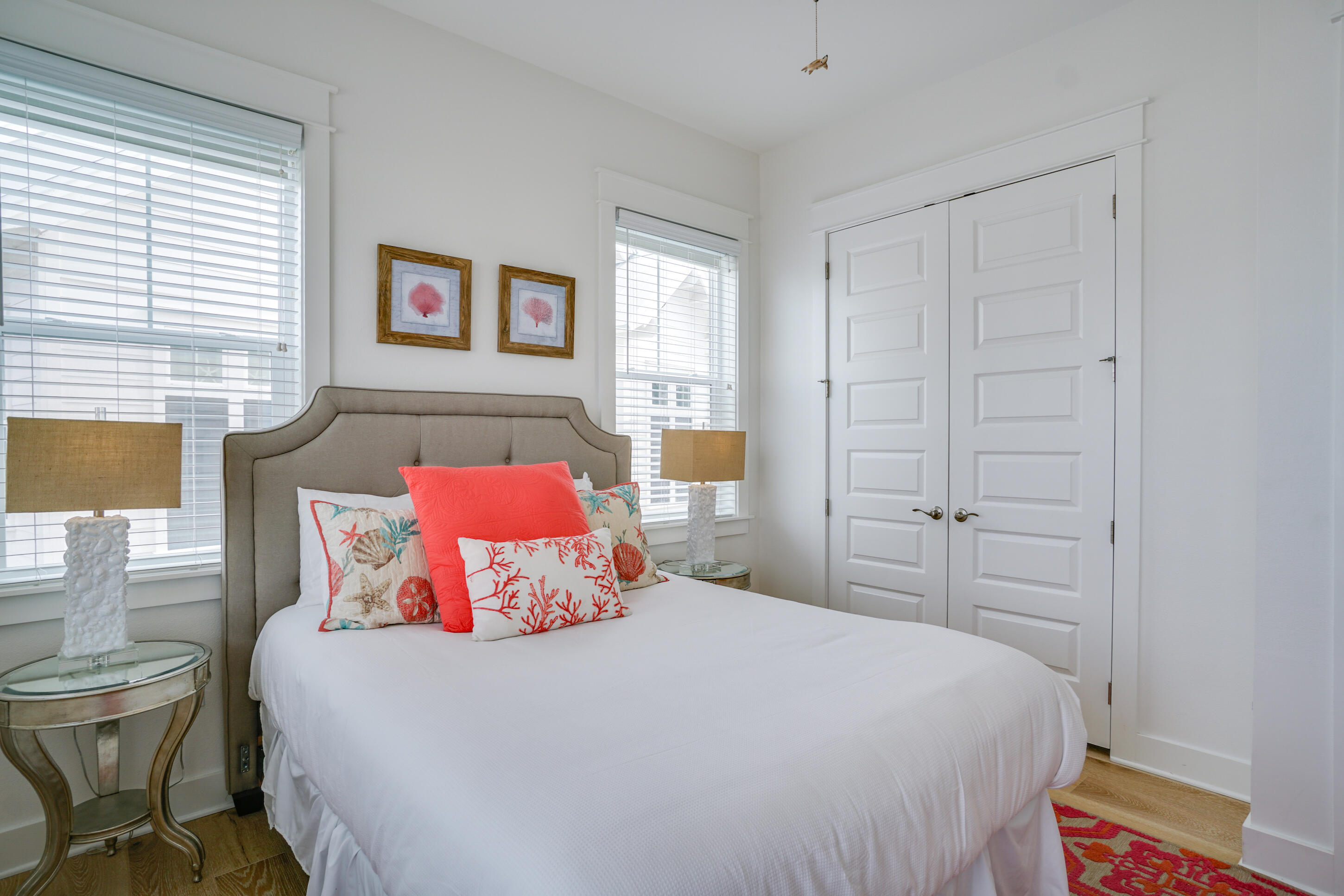 Bright bedroom with coral accent pillows, a gray upholstered headboard, and white double doors.
