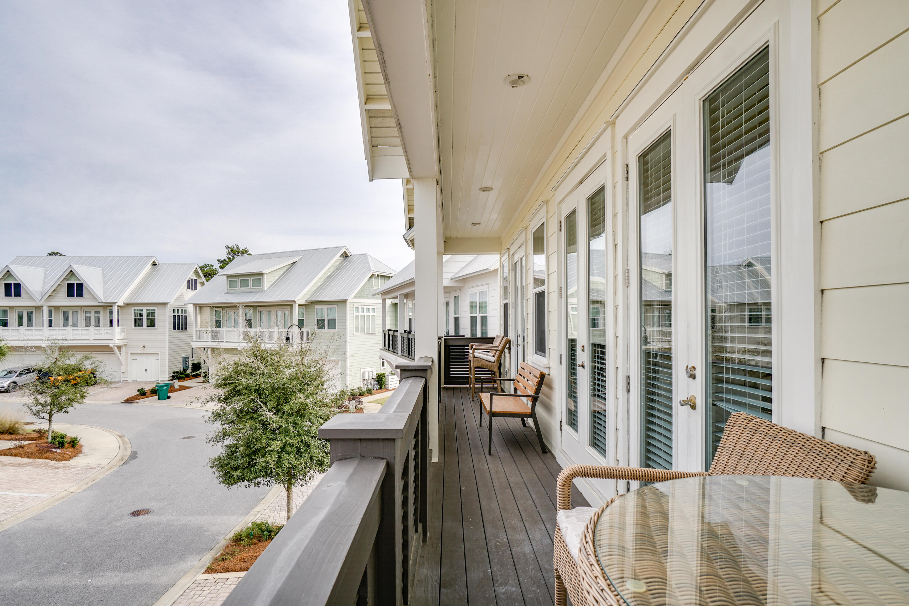Covered balcony with wicker seating overlooking a quiet street and neighboring homes.
