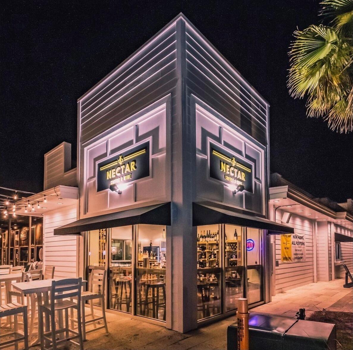 Nectar Coffee & Wine storefront at night, with illuminated signs and outdoor seating.