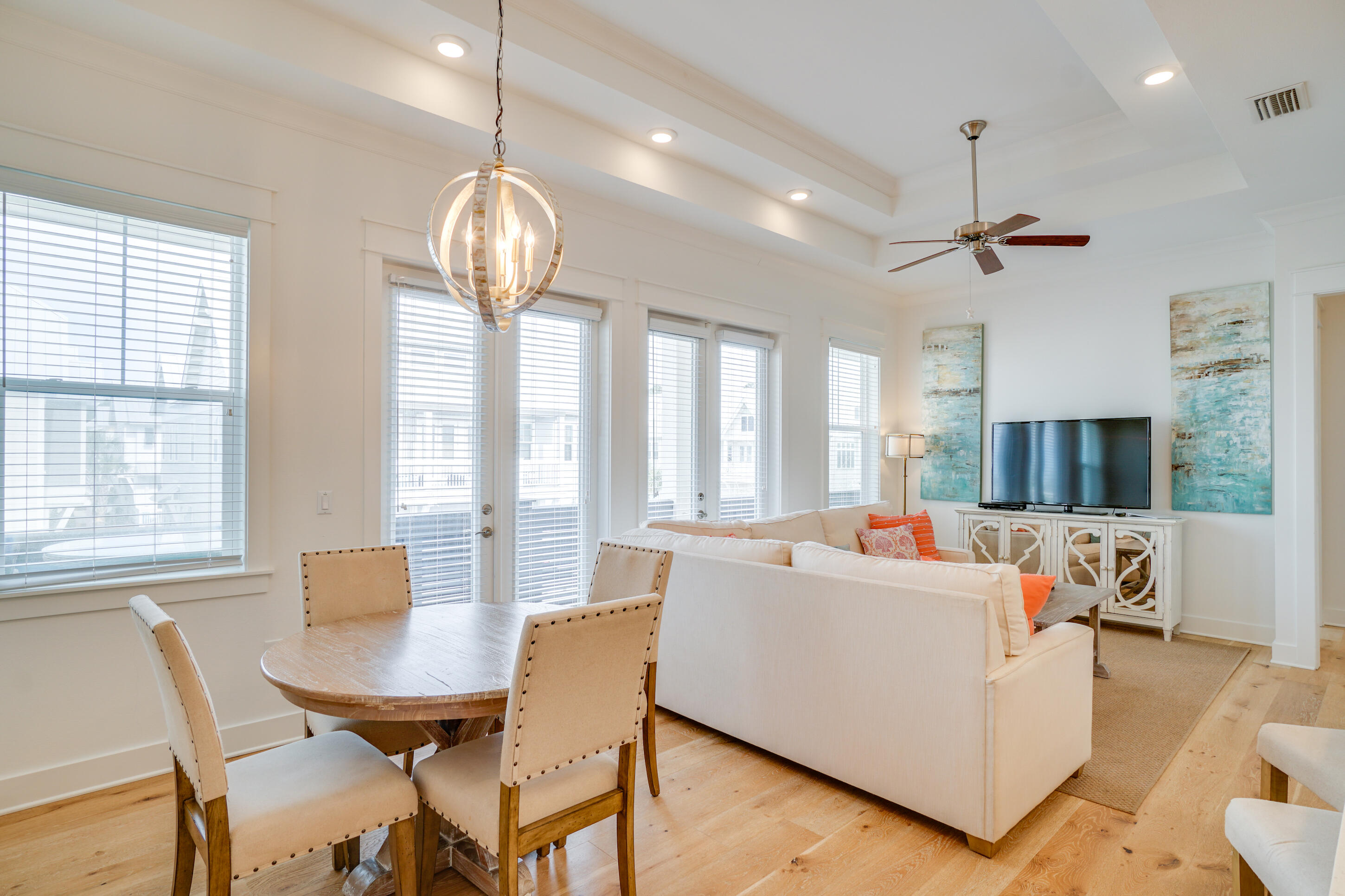 Open-plan living and dining room with a white sofa, round table, large windows, and light wood floors.