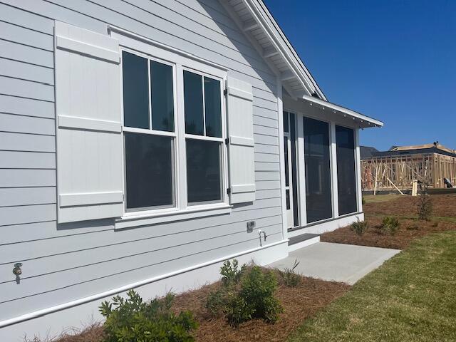 Light gray home with white-trimmed windows, sliding glass doors, and a concrete patio beside a grassy lawn.
