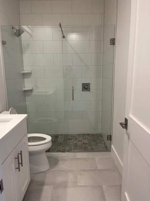 Bathroom with a glass-enclosed tiled shower, white vanity, and toilet.