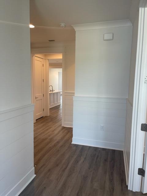 Hallway with white wainscoting and dark wood-look flooring leading to a bathroom vanity.