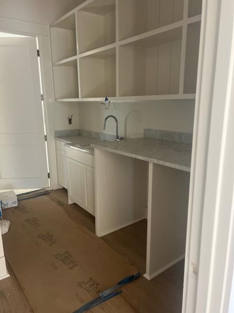 Laundry room with a gray counter and sink, white cabinetry, open cubbies, and unfinished flooring.