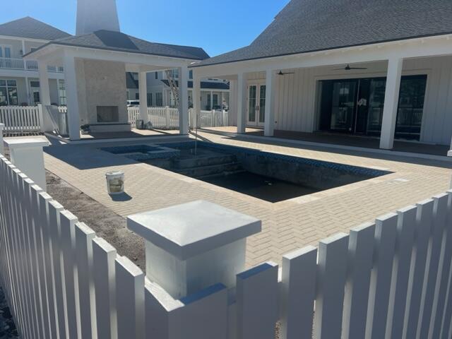 White coastal-style home surrounding an empty pool, with a paved patio and outdoor fireplace.