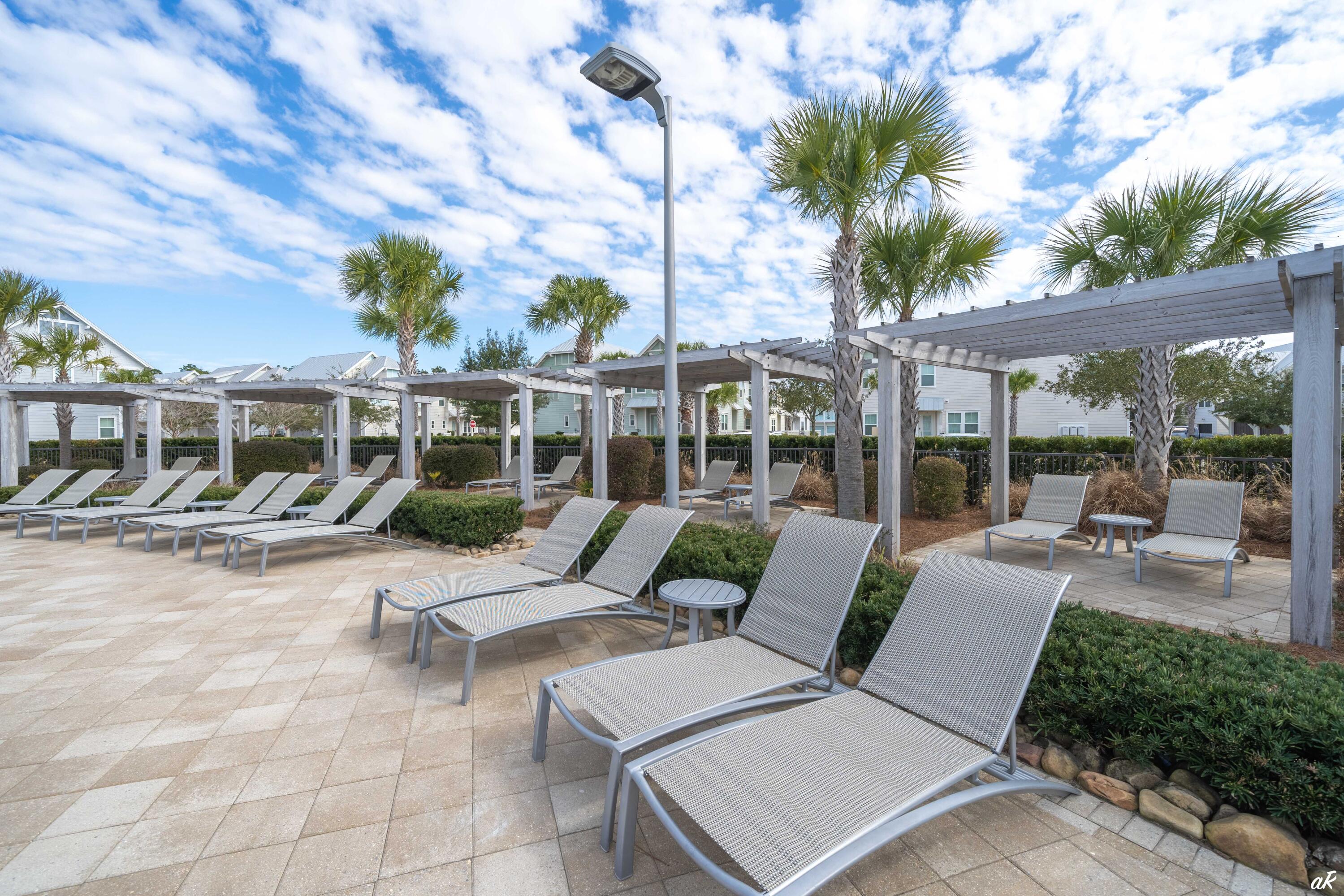 Outdoor patio with rows of lounge chairs beneath pergolas and palm trees.