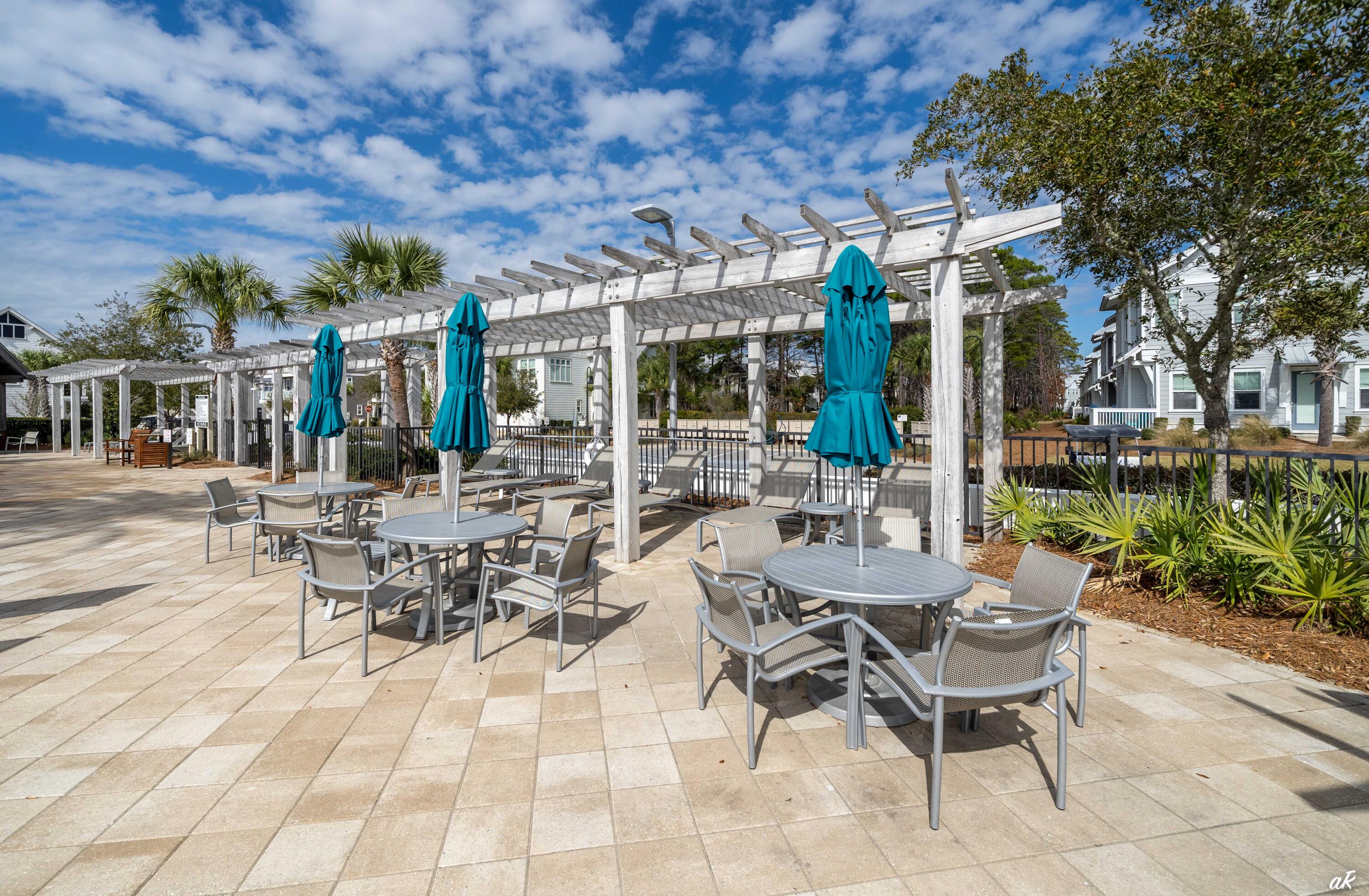 Outdoor patio with a white pergola, café seating, and closed teal umbrellas.
