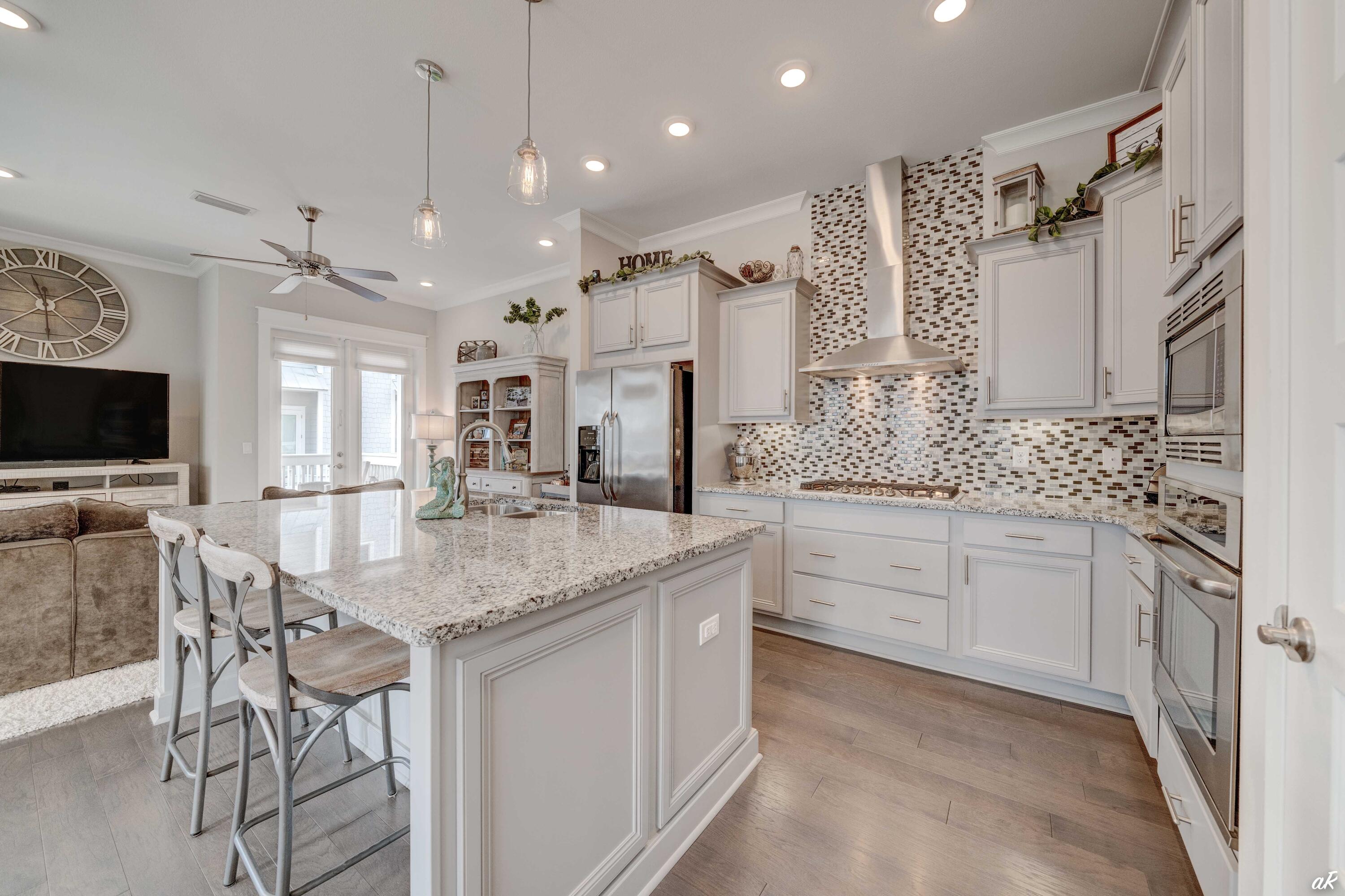 Open-plan kitchen with a large granite island, white cabinets, and mosaic tile backsplash.