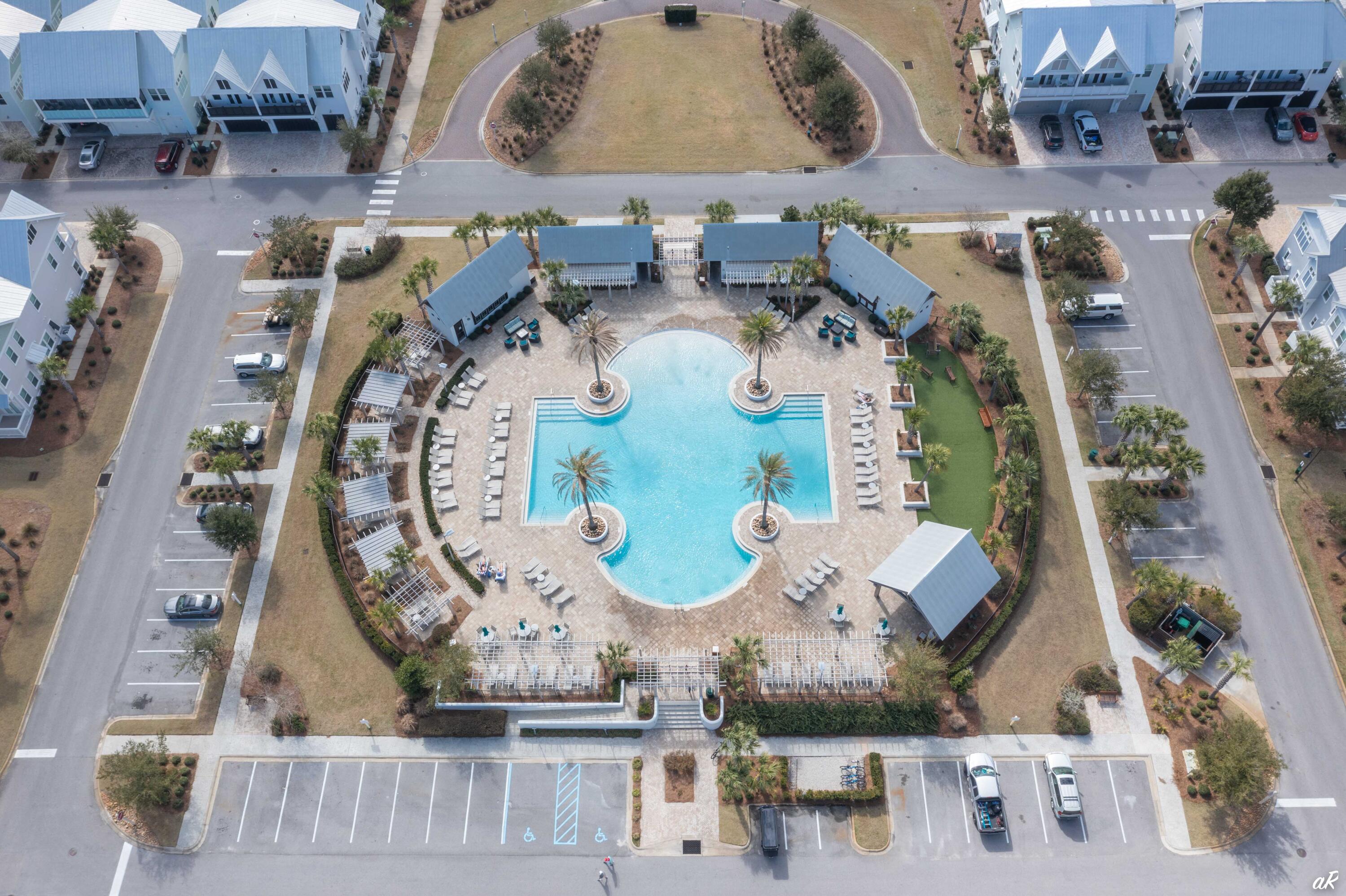 Aerial view of a resort-style pool surrounded by palm trees, lounge chairs, and pergolas.