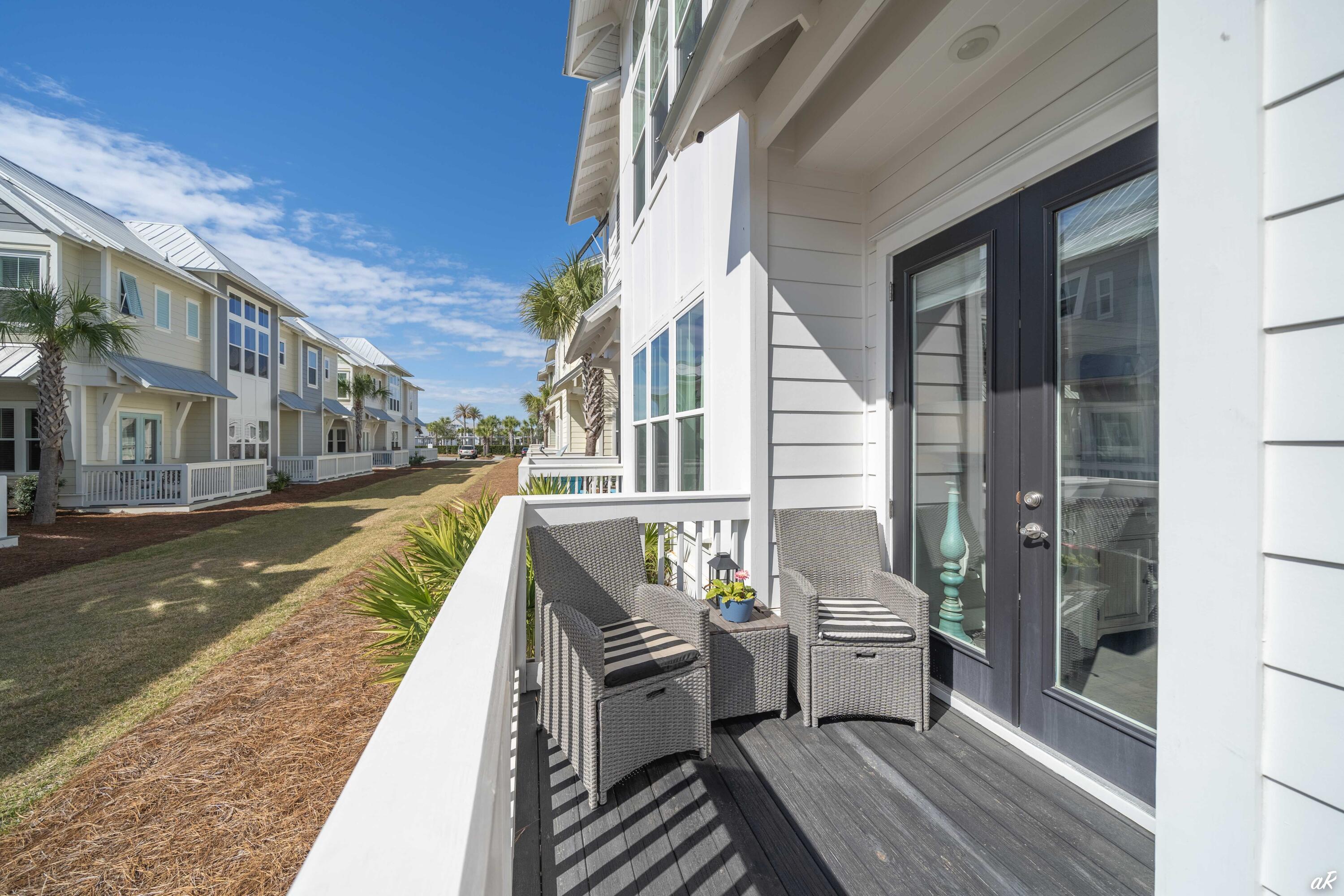Furnished porch with wicker chairs overlooking a lane lined with coastal-style homes.