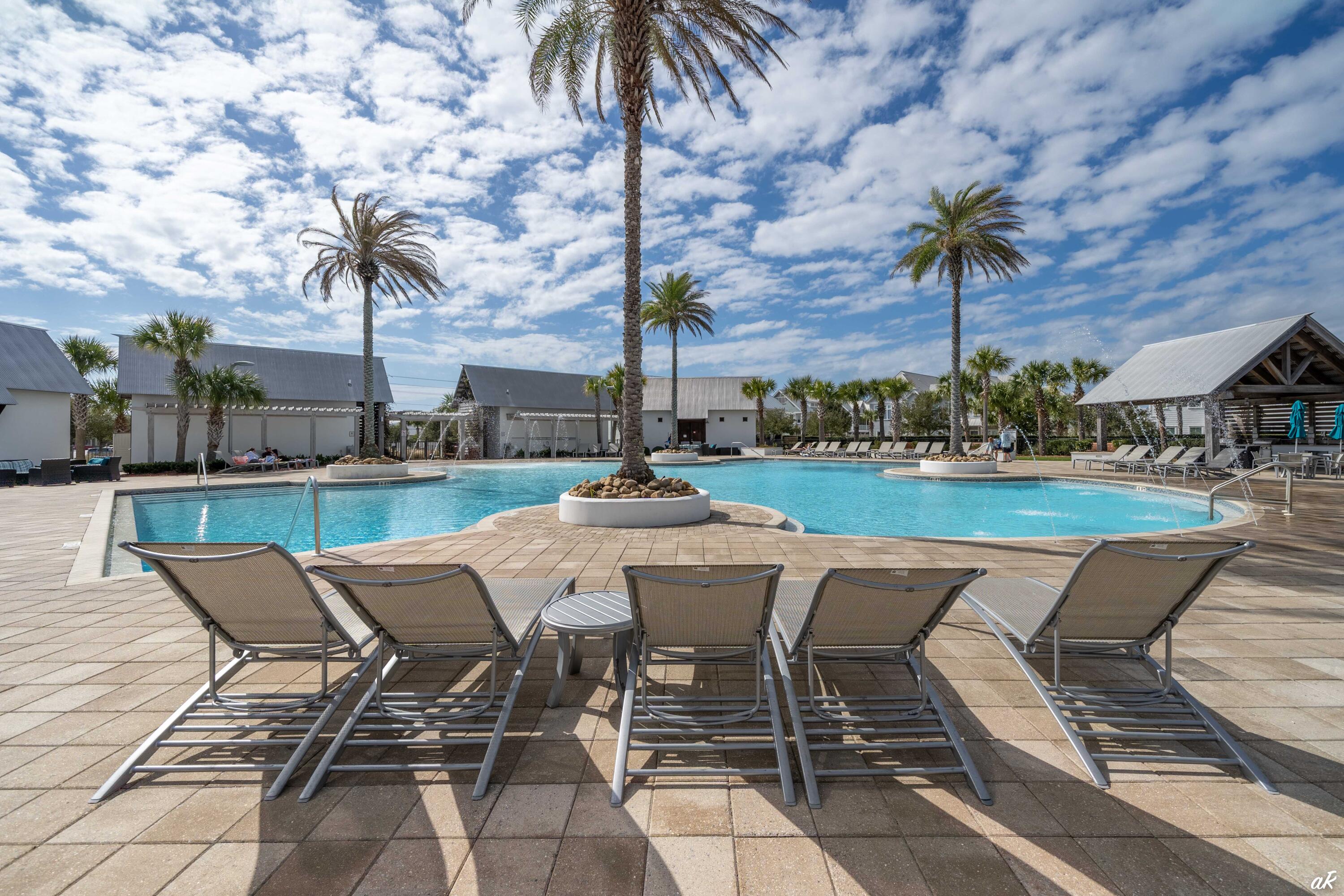 Outdoor pool with palm trees, covered cabanas, and lounge chairs on the paved deck.