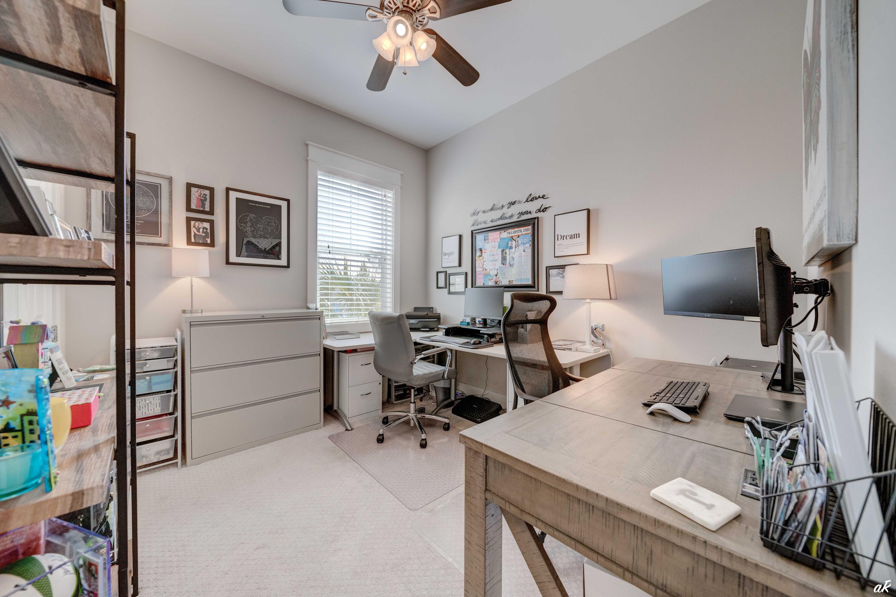 Home office with two workstations, wooden desks, computer monitors, and framed wall art.