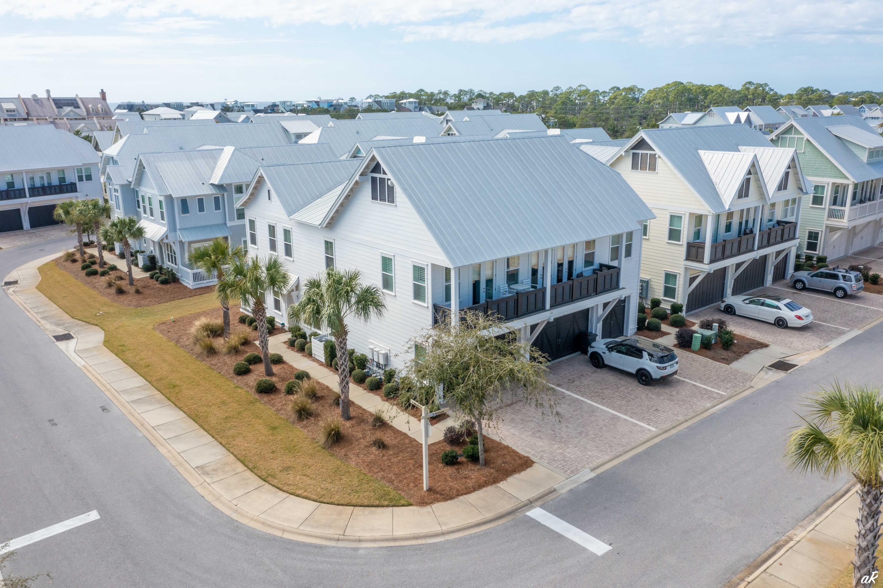 White corner townhouse with a metal roof, balconies, palm trees, and nearby homes, viewed from above.