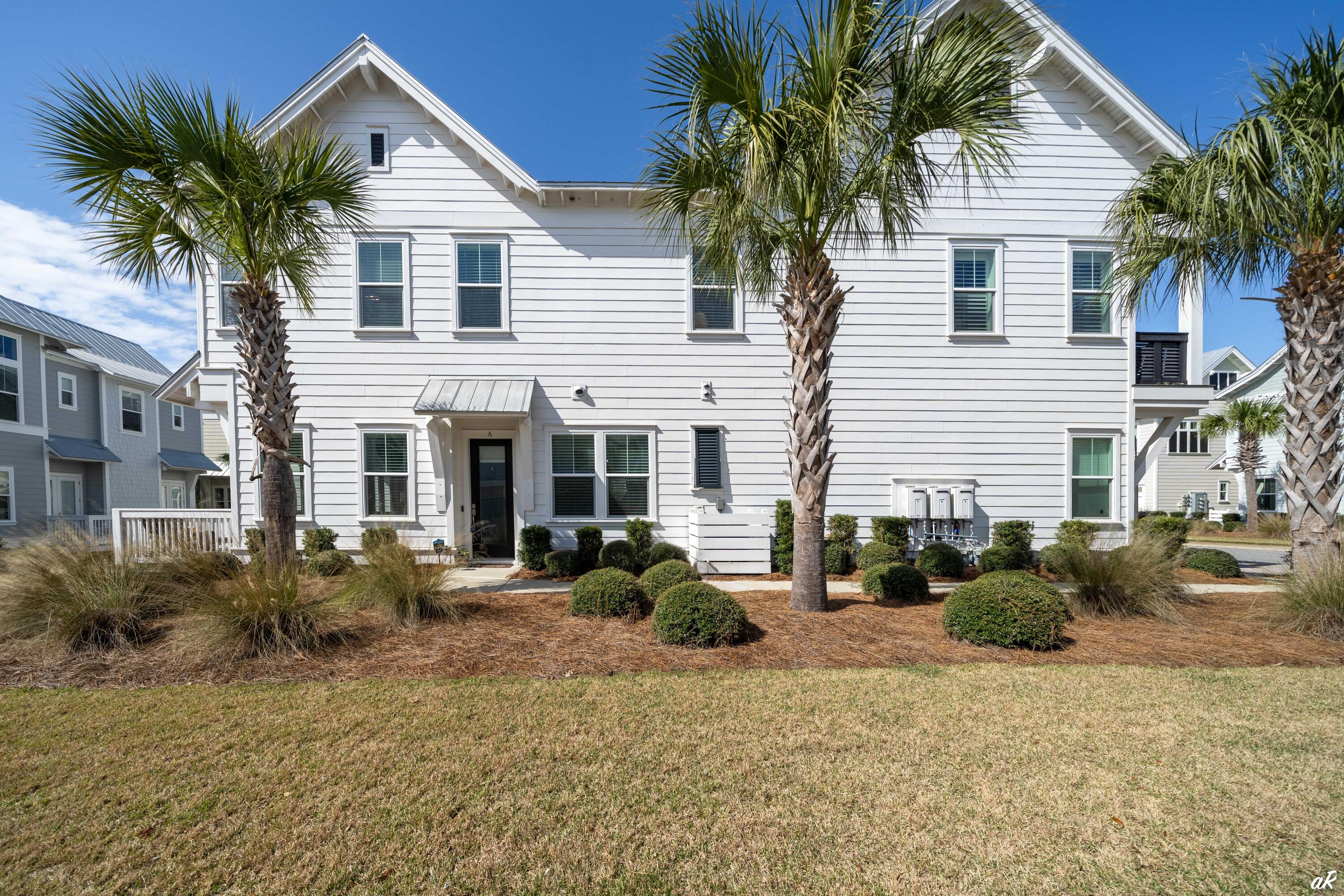 White two-story home with a covered entrance, palm trees, and landscaped lawn.