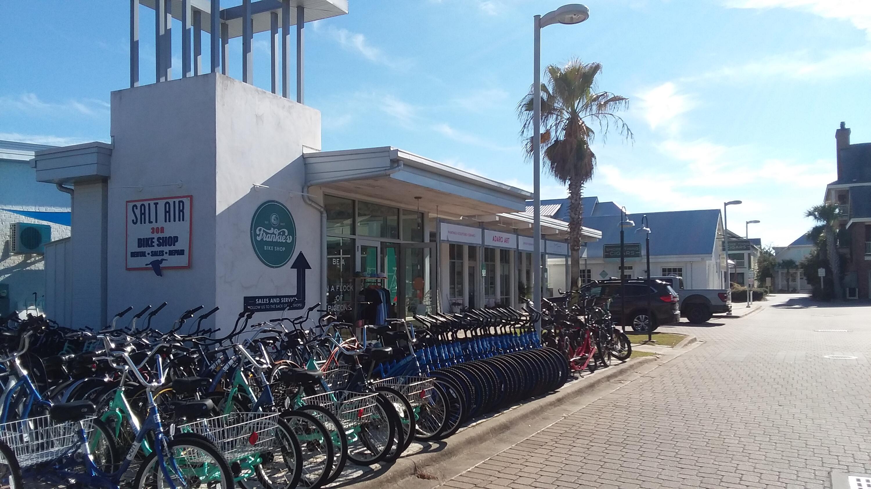 Bike shop storefront with rows of bicycles parked outside along a sunny street.