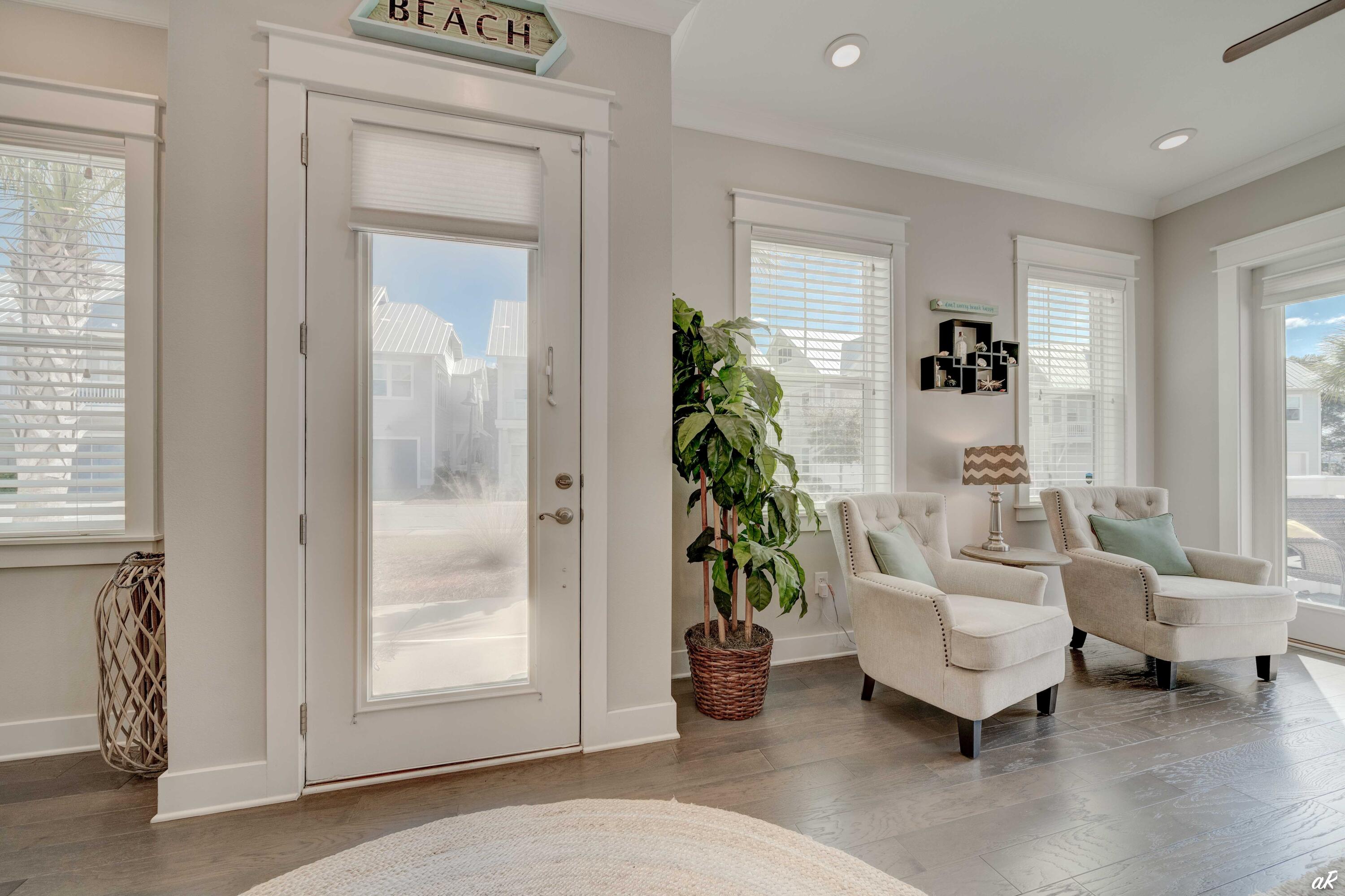 Bright living room with cream armchairs, a potted tree, and a glass-paneled entry door.