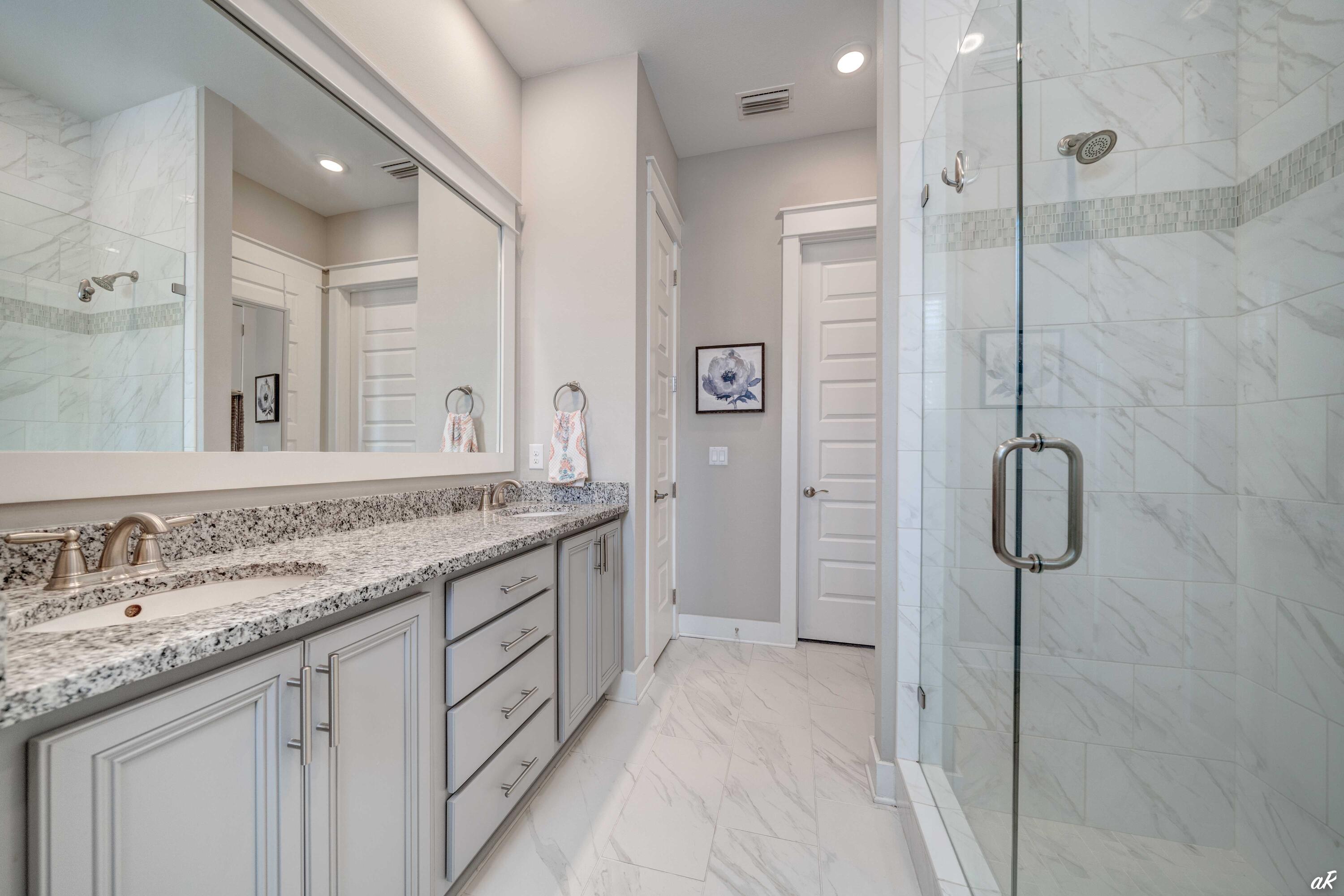 Bathroom with a granite double vanity and glass-enclosed marble-look shower.