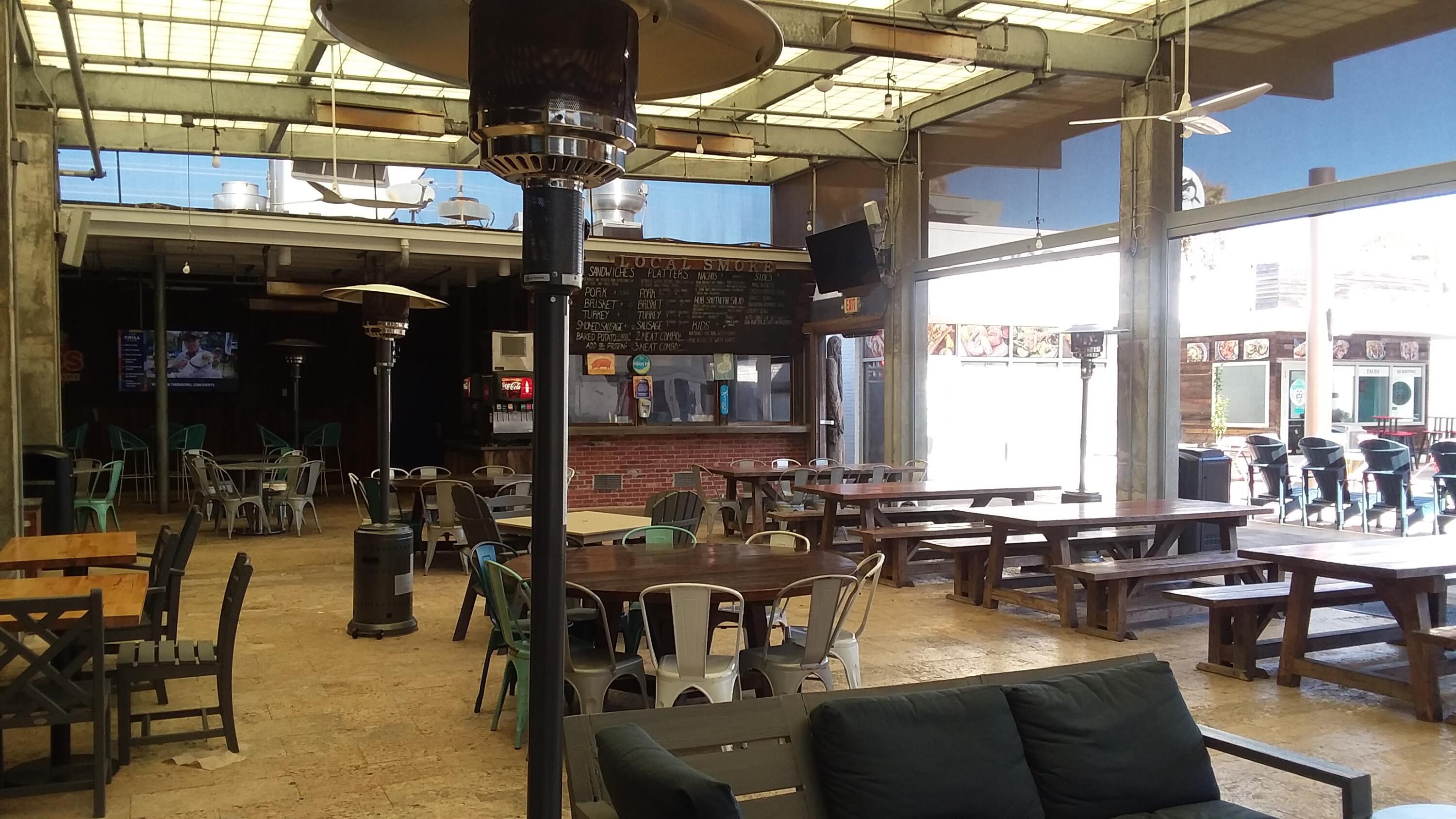 Restaurant dining area with picnic tables, metal chairs, patio heaters, and a LOCAL SMOKE counter.