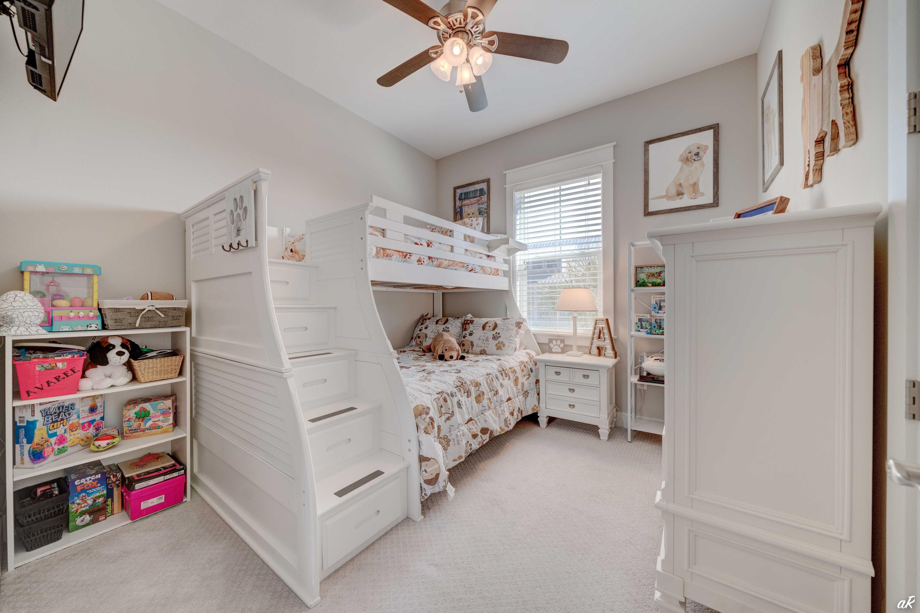 Children’s bedroom with a white staircase bunk bed, patterned bedding, and shelves of toys.