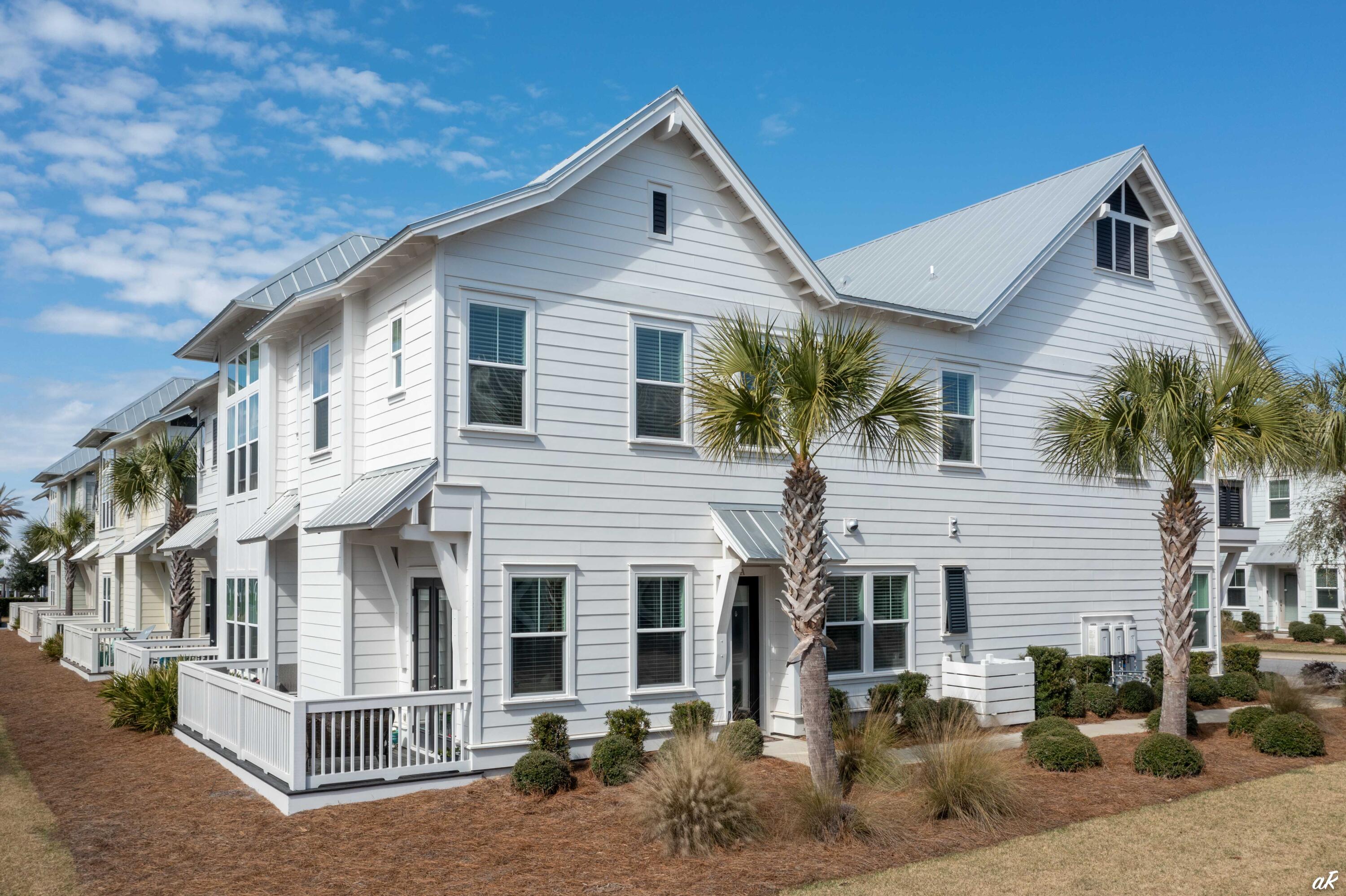 White coastal-style building with metal gabled roofs, porches, and palm trees.
