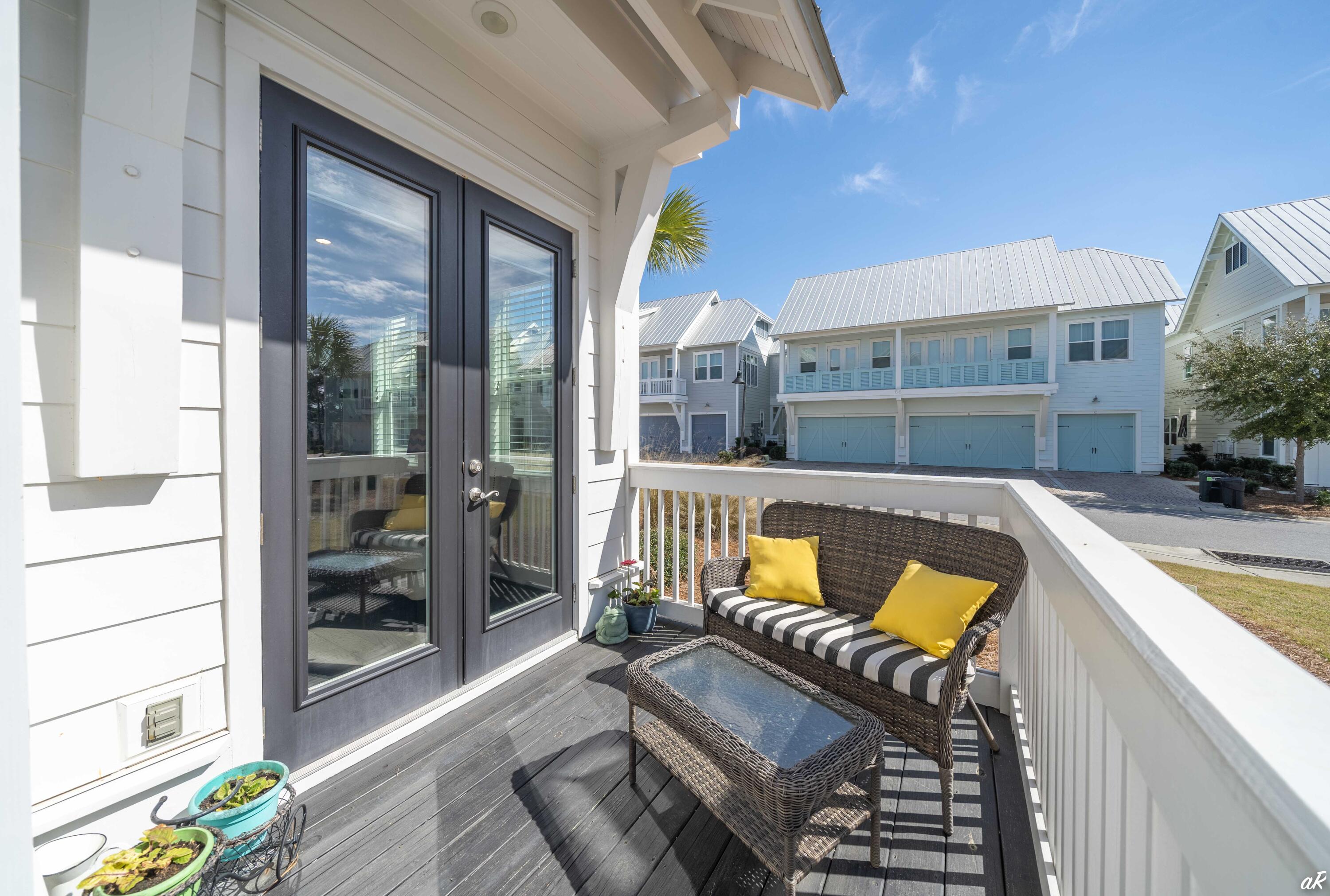 Furnished porch with wicker seating and yellow cushions overlooking neighboring coastal homes.